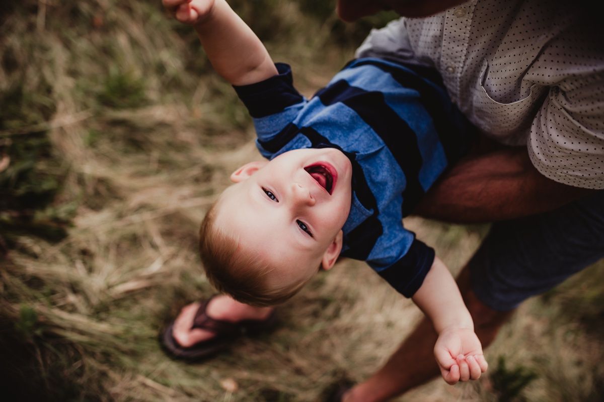 Joyful child laughs while being held upside down outdoors.