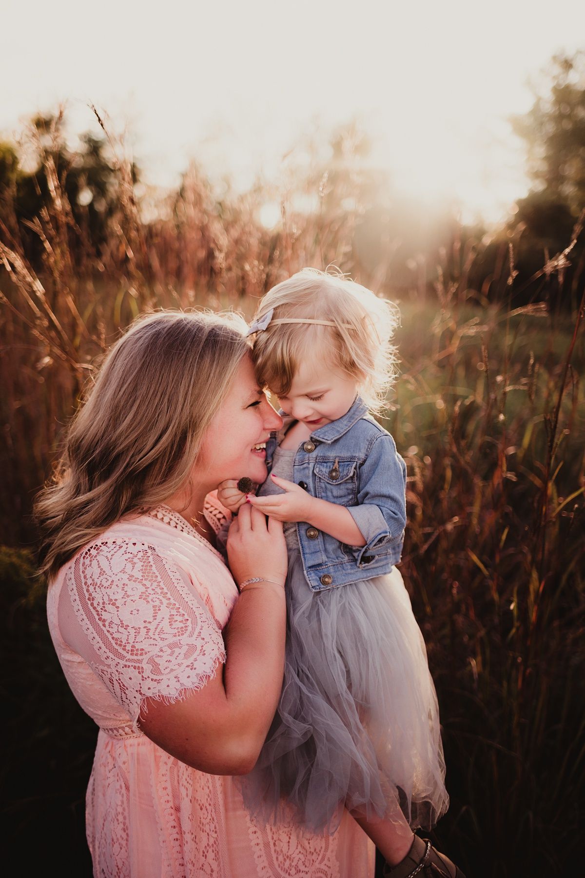 Tender moment between parent and child in pink dress against sunset-lit field.