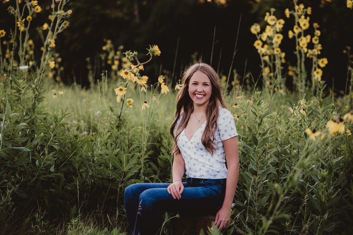 Candid lifestyle portrait in tall wildflowers during golden hour with casual summer attire.