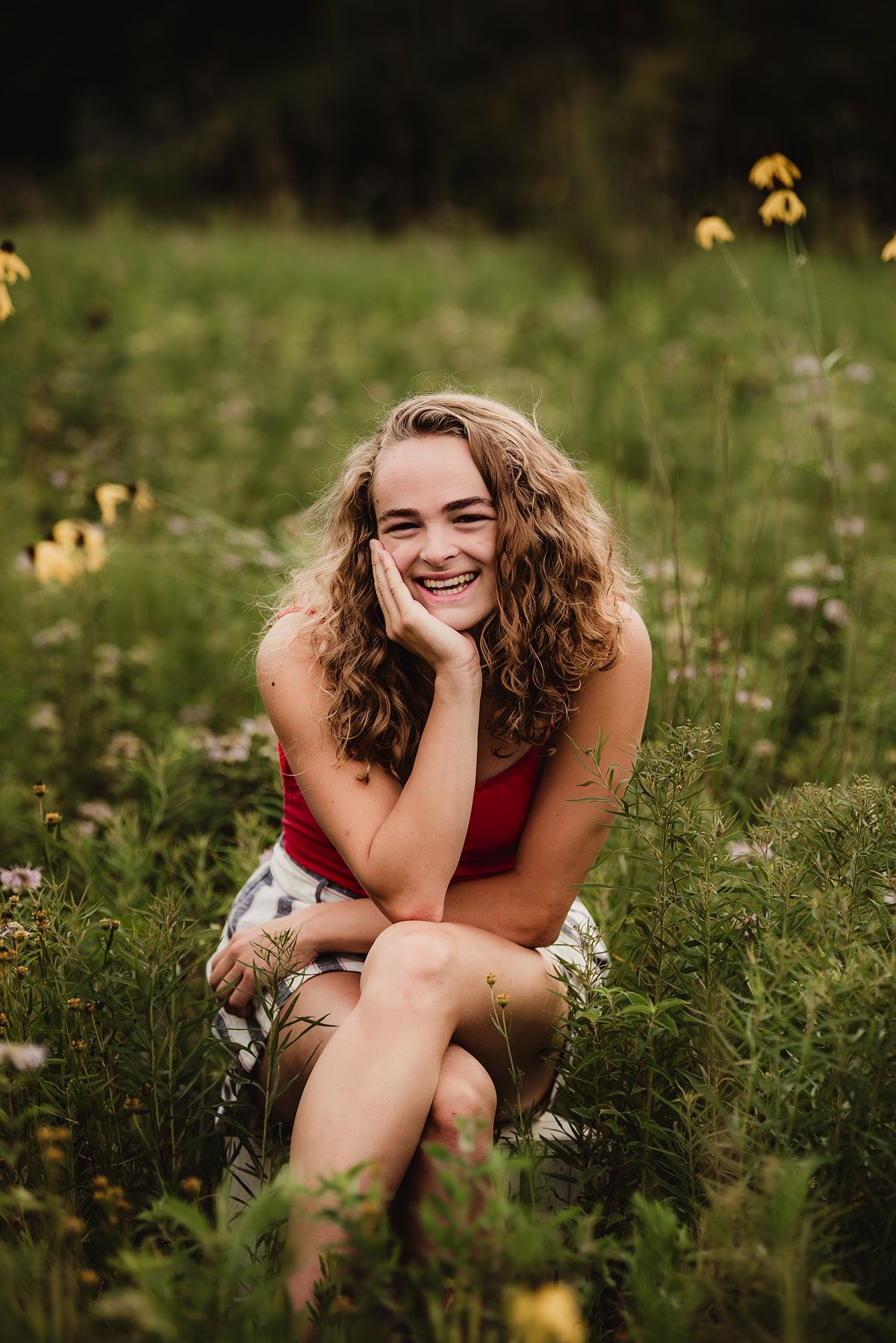 Joyful summer portrait amidst wildflowers and tall grass wearing red tank top and striped shorts.