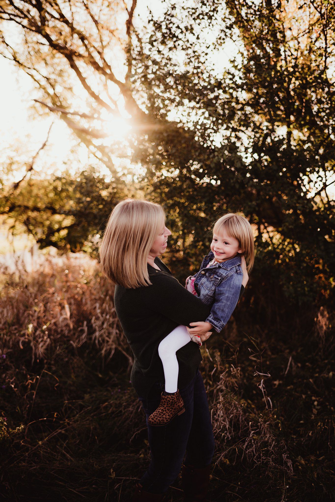 Two people share a loving moment outdoors with sunlight streaming through tree branches.