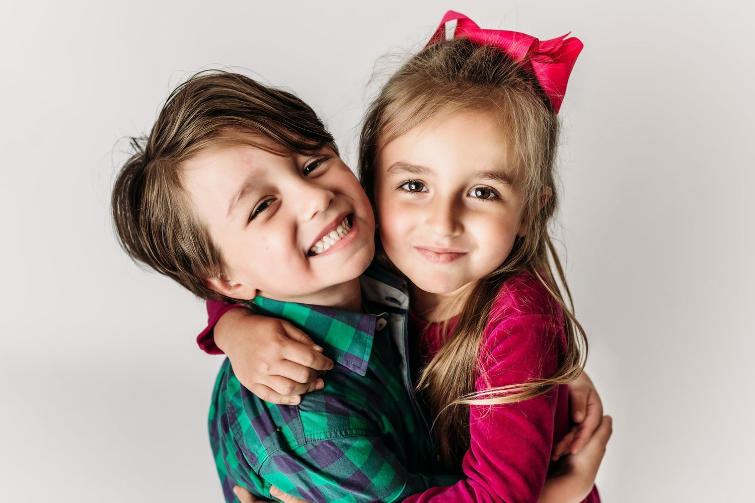 Two children in festive outfits embracing and smiling against white backdrop.