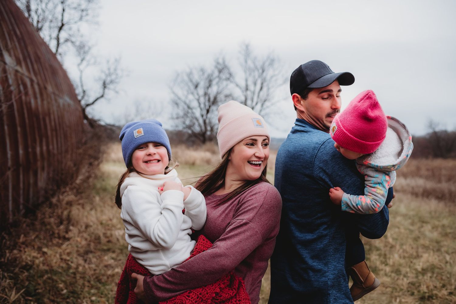 Outdoor family portrait in winter clothing against weathered metal barn structure.
