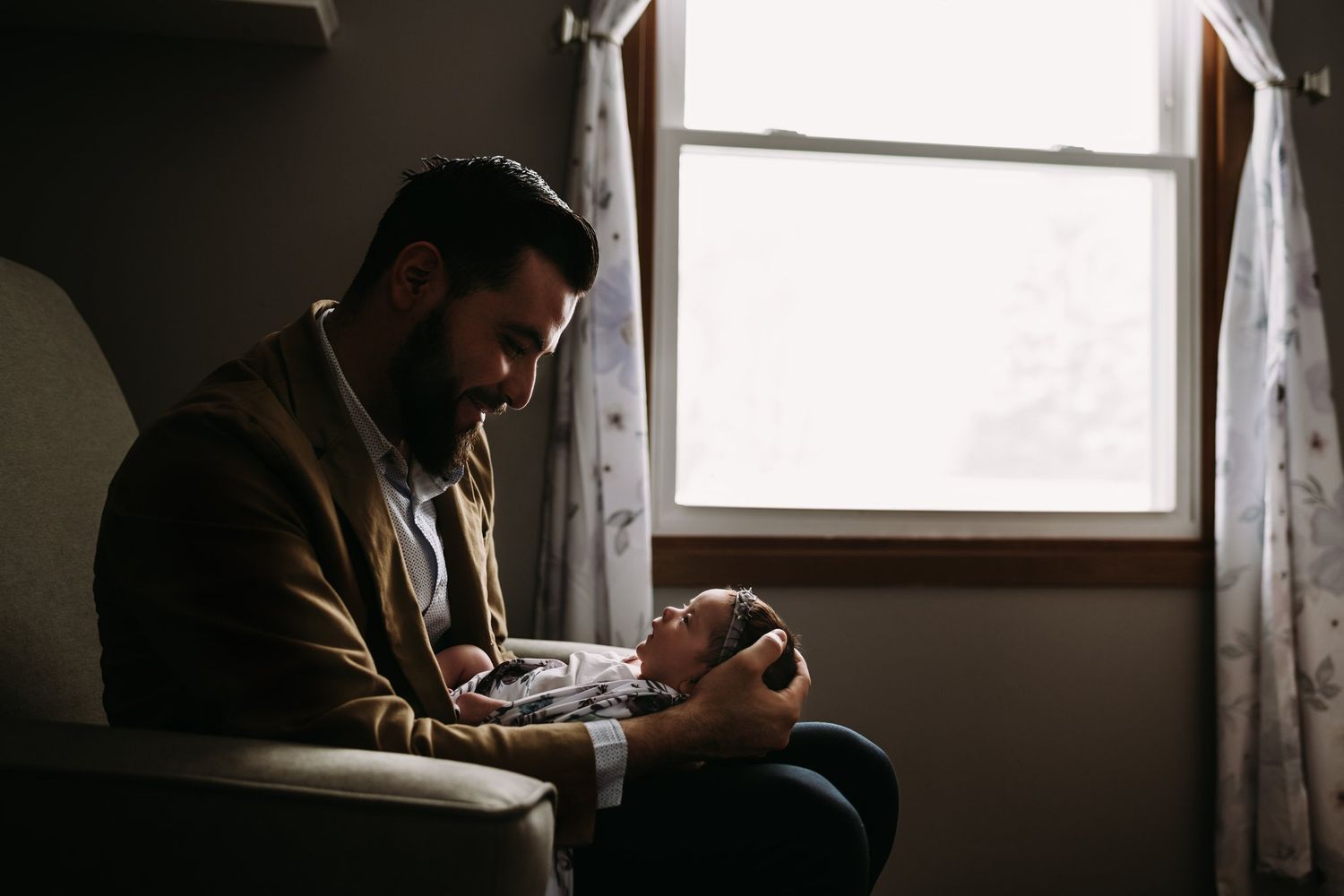 Person sitting by window holding newborn baby in soft natural light.