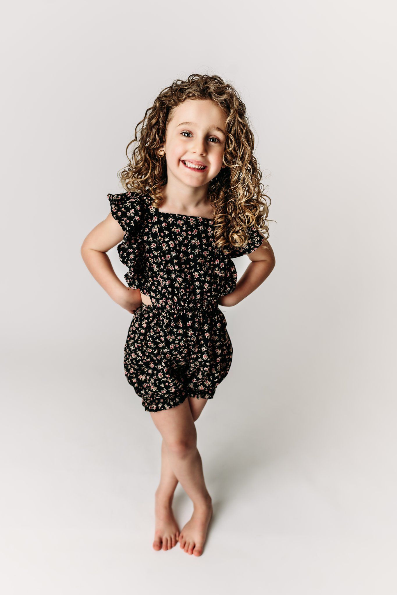 A child in a black floral romper poses playfully against a white background.