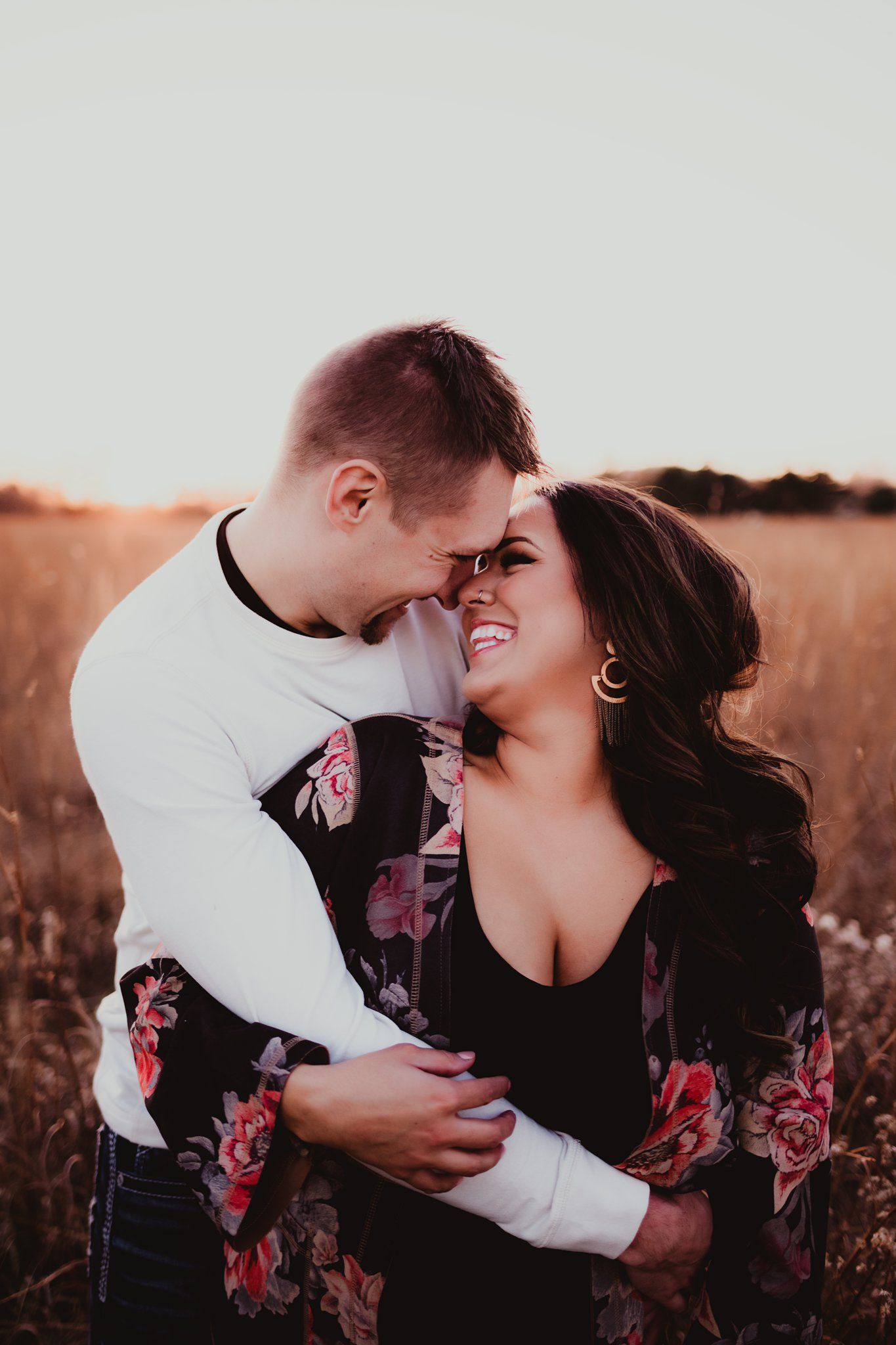 Couple sharing intimate moment in field during sunset while wearing floral and white outfits.