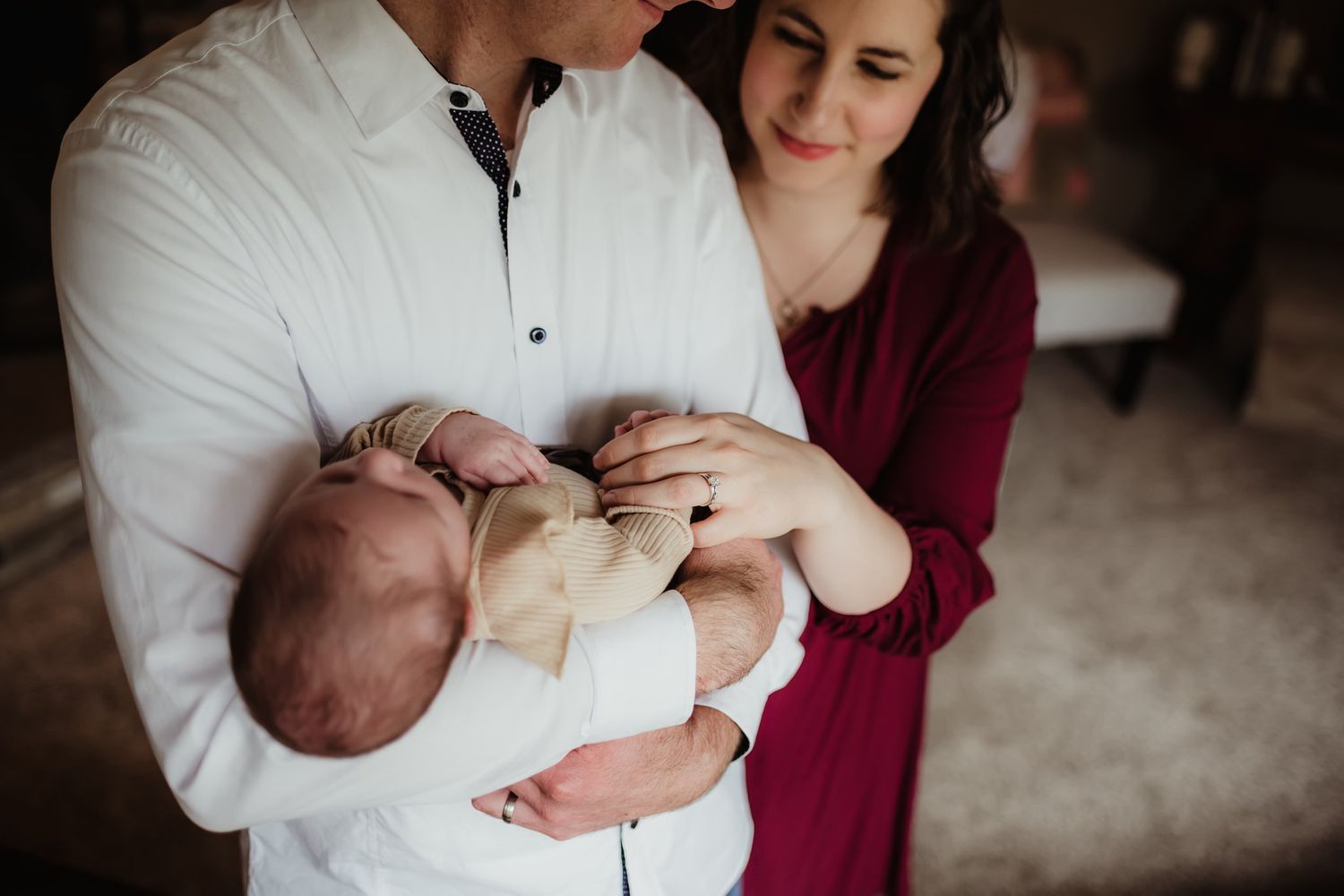 Couple in white shirt and burgundy dress tenderly holding their newborn baby.