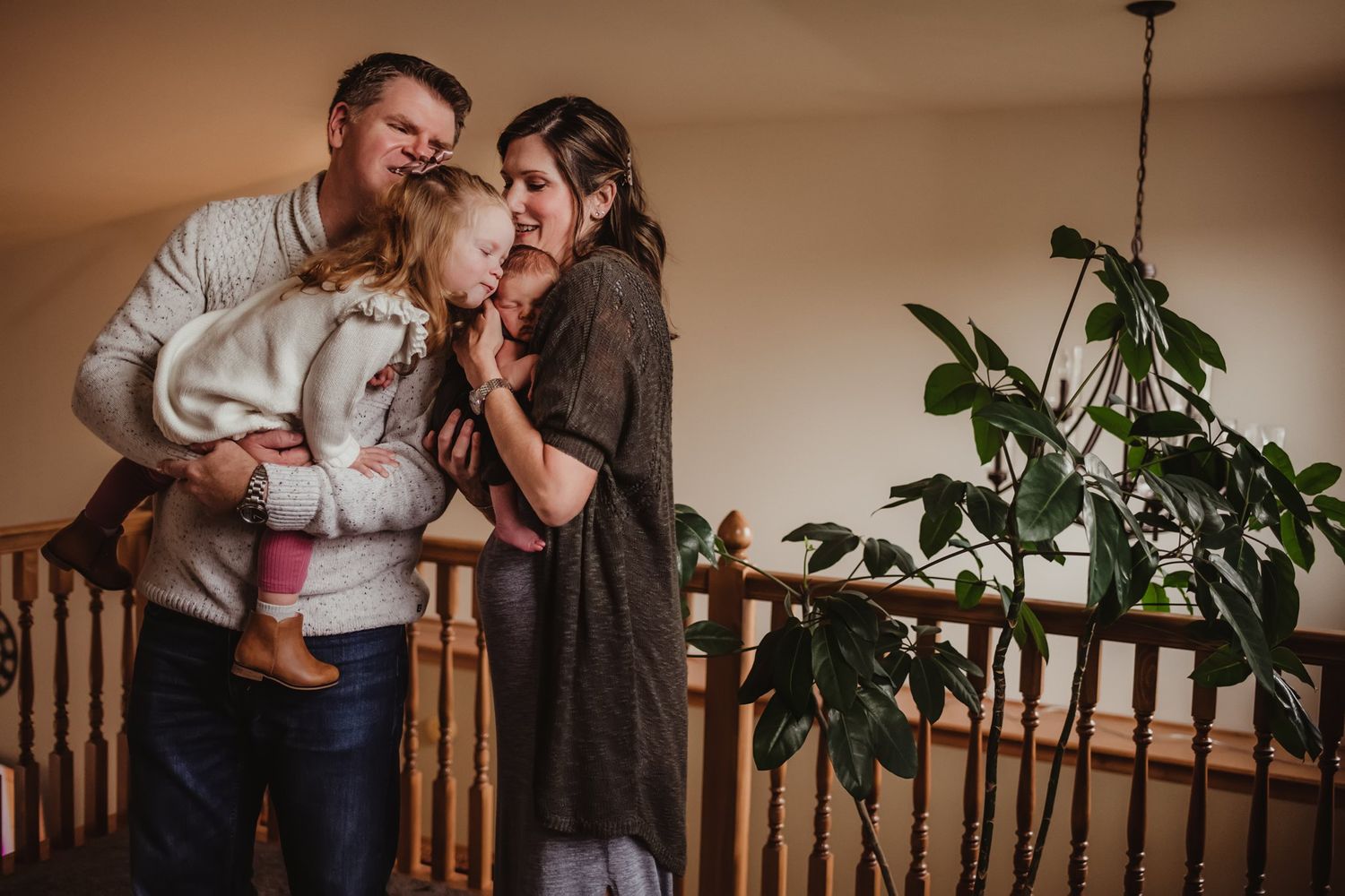 Warm family moment captured indoors with houseplants and wooden banister in background.