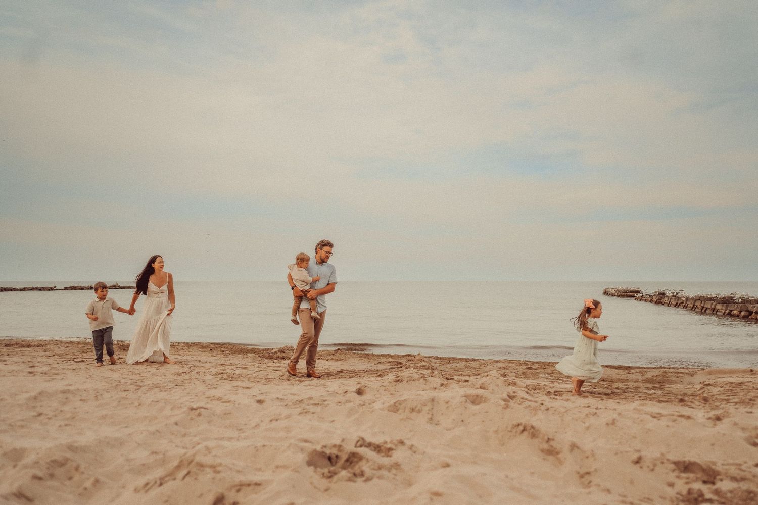 Family members spread out playing on a sandy beach during sunset.