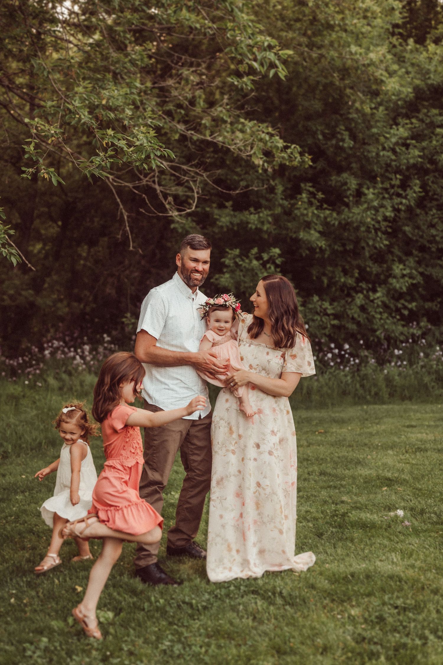 A family shares a joyful moment together on a grassy lawn surrounded by trees.