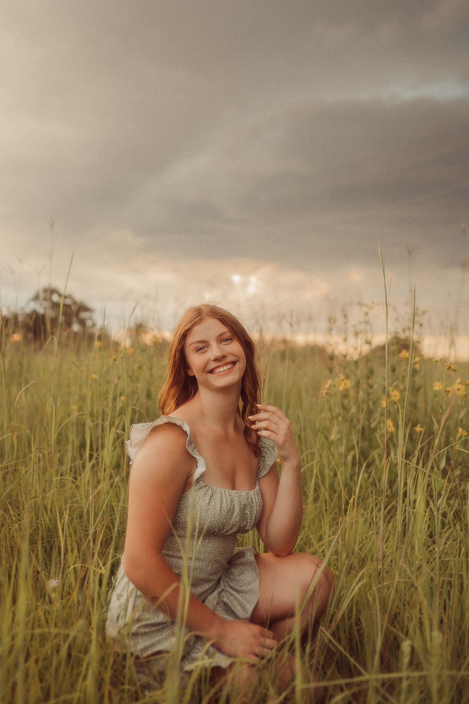 Candid summer portrait in tall grass under dramatic cloudy skies.