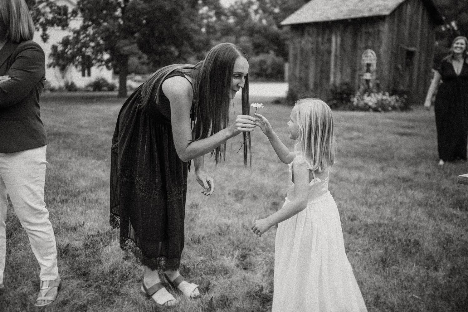 A black and white photo of two people interacting on a grassy field with a barn in the background.