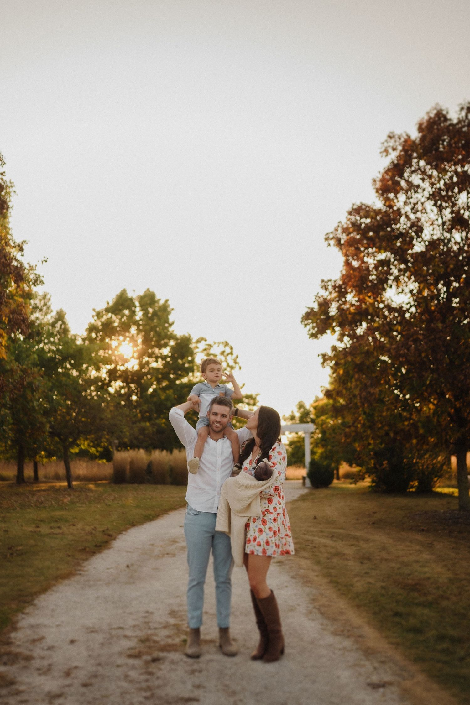 Family enjoying sunset moment on dirt path surrounded by autumn trees.