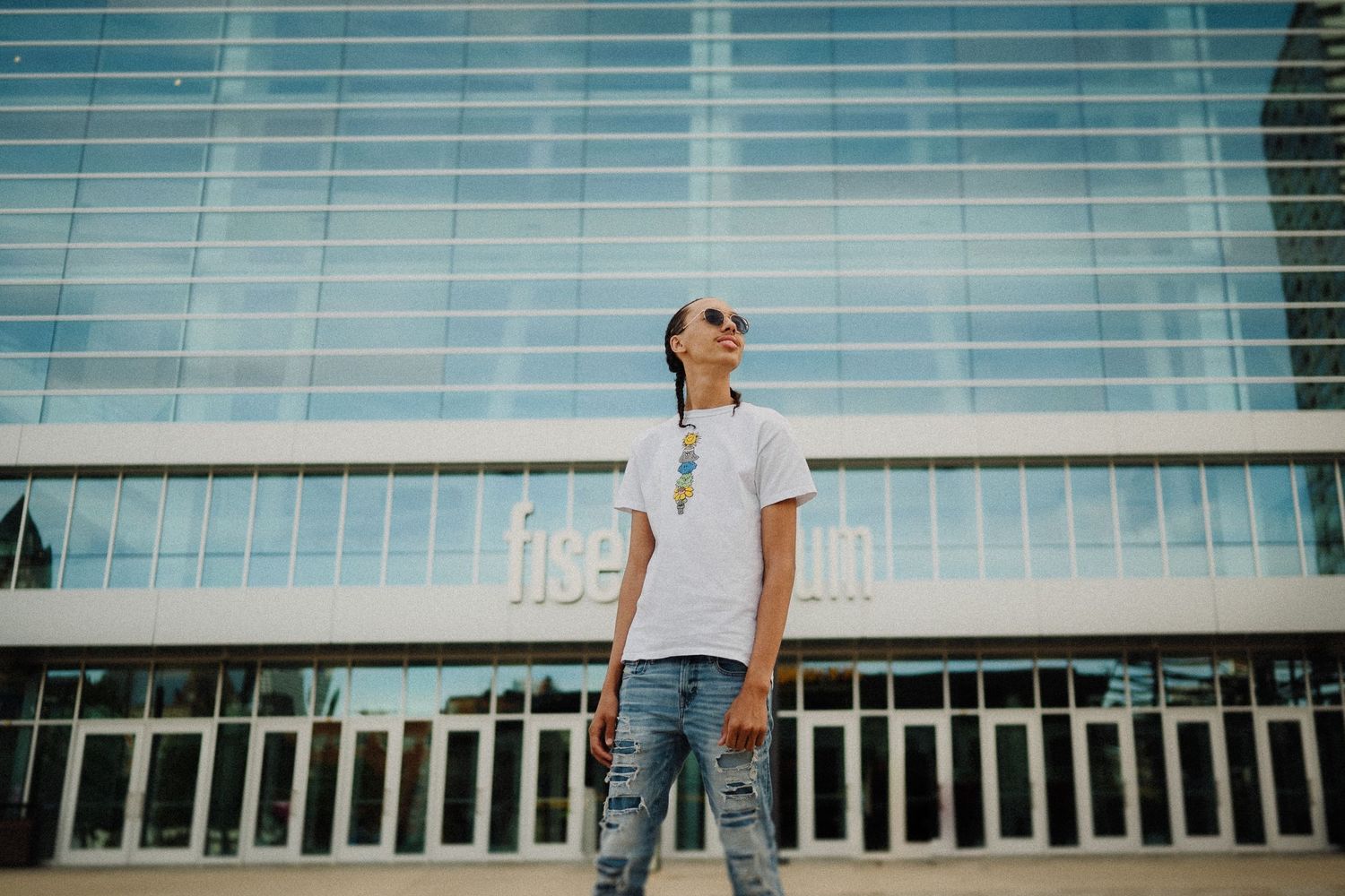 Person standing in front of modern glass building on sunny day.