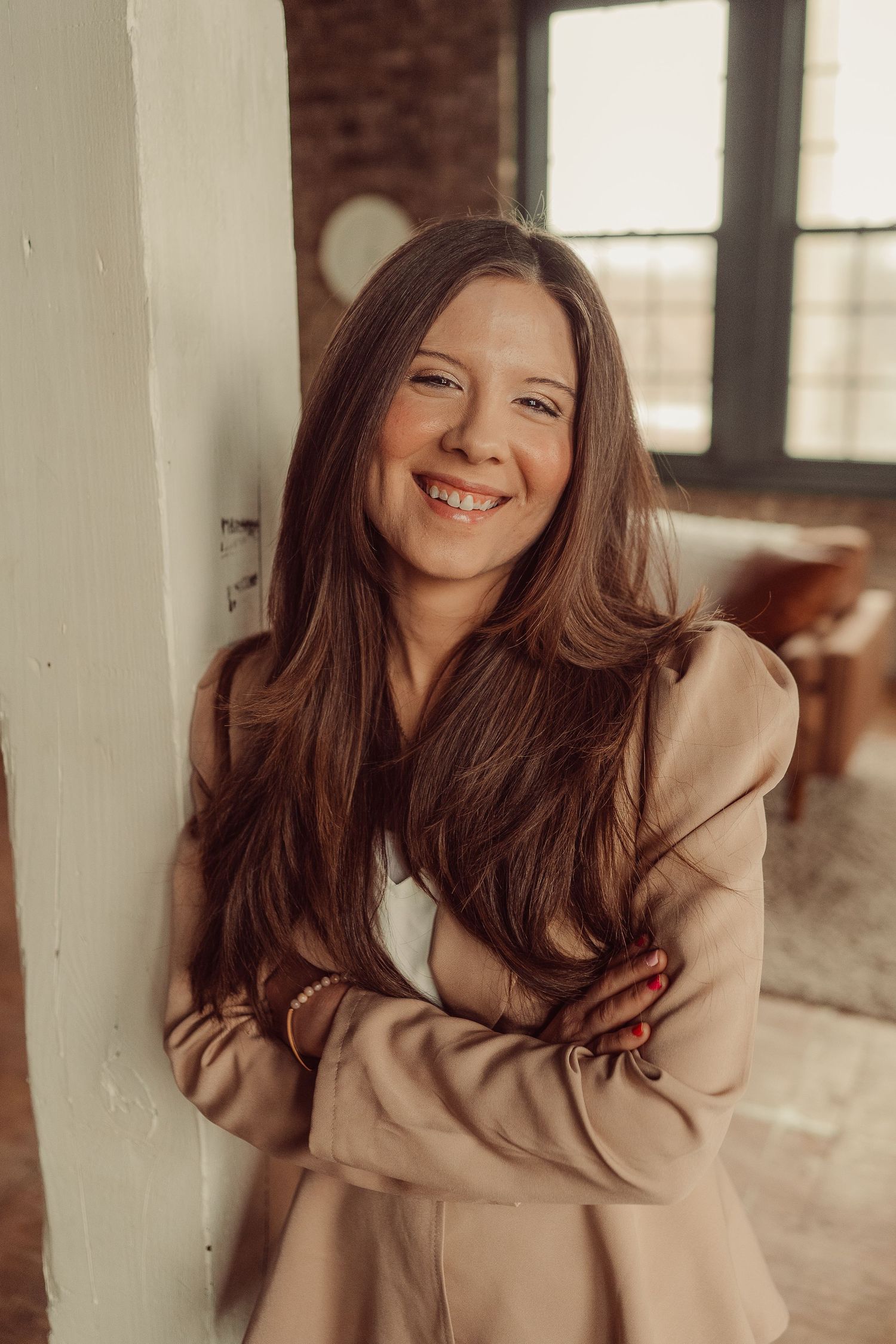 Warm candid portrait against white wall showing genuine smile and professional style.