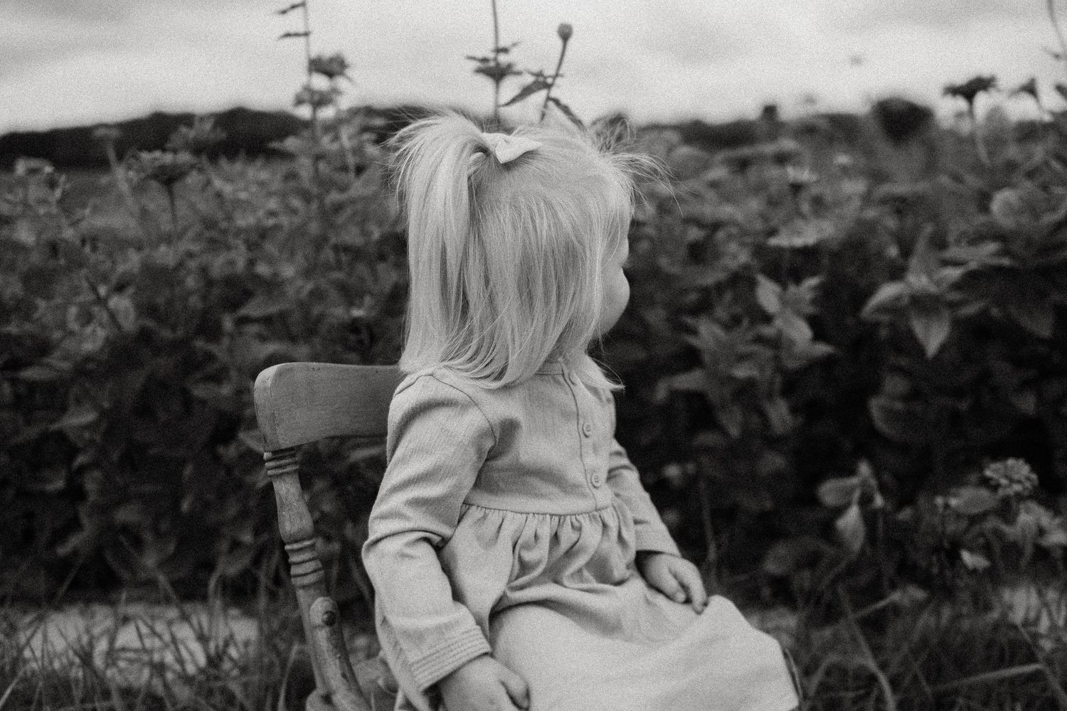 Black and white image of someone sitting on wooden chair looking at garden flowers.