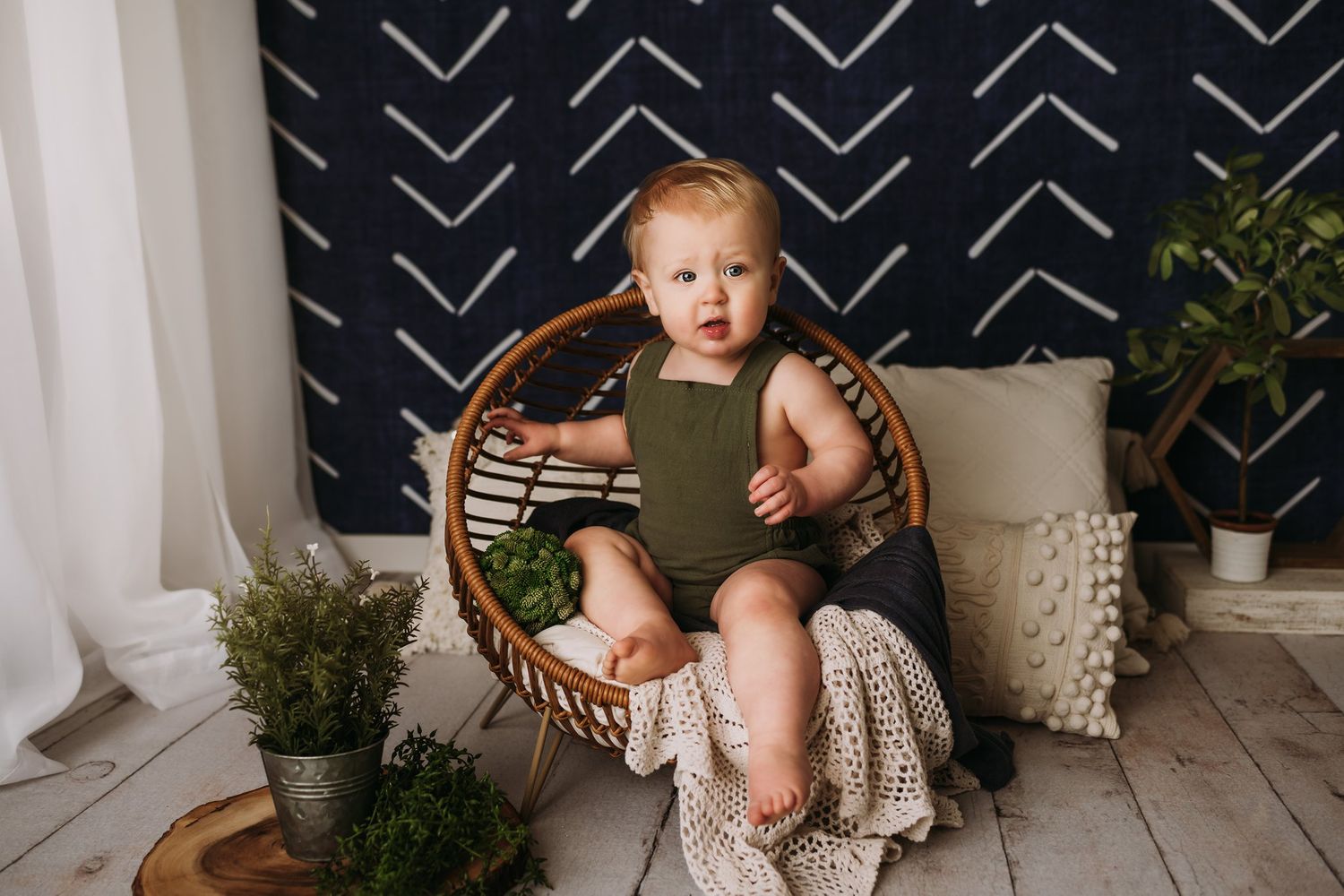 A cozy portrait setting with a round rattan chair and cream blanket against a geometric navy wall.