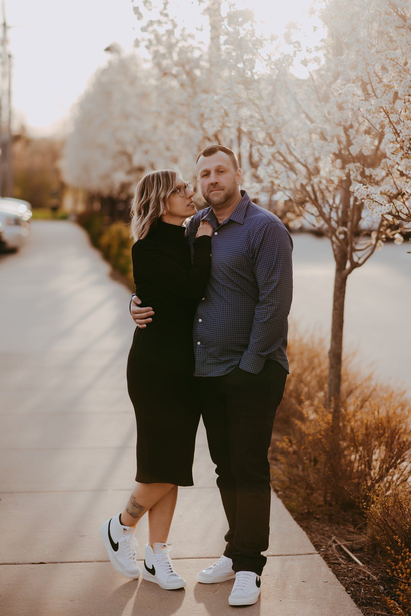Couple in casual wear sharing affectionate moment on sidewalk with blooming trees.