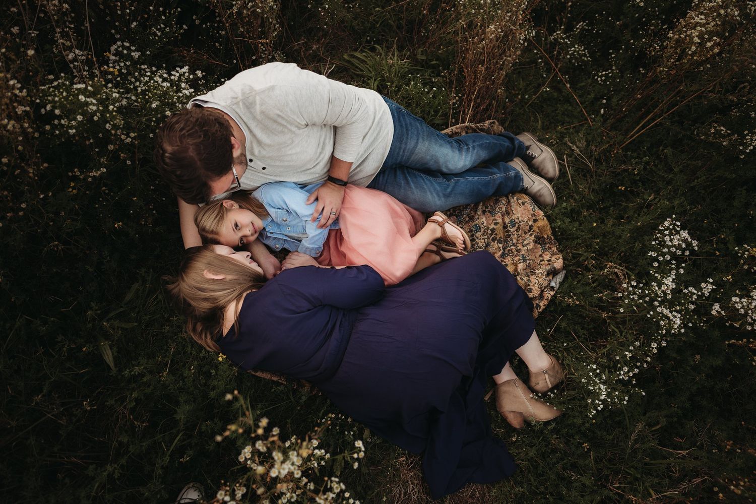 Family lying together in a field of wildflowers during an outdoor photo session.