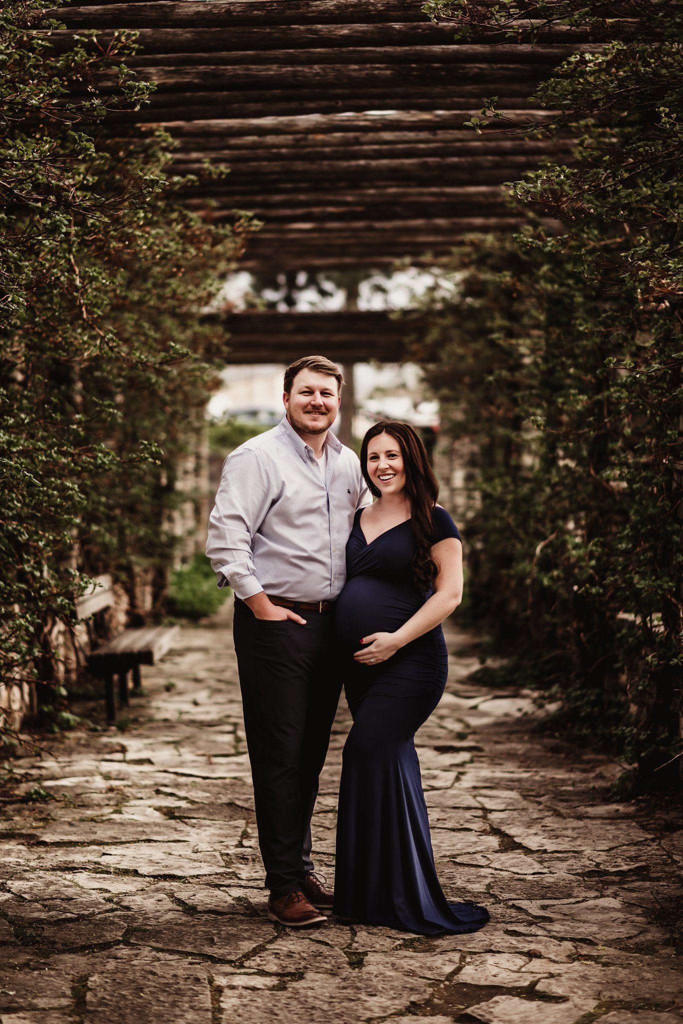 Elegant maternity portrait of couple in formal wear under stone archway.