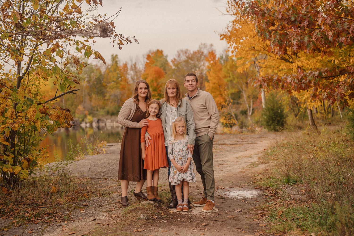 A group poses together on an autumn path surrounded by vibrant orange and yellow fall foliage near a lake.