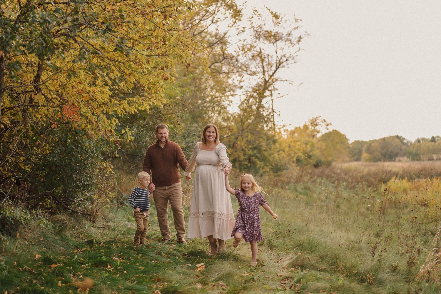 A group walks together through a golden sunlit field during an autumn sunset photo session.