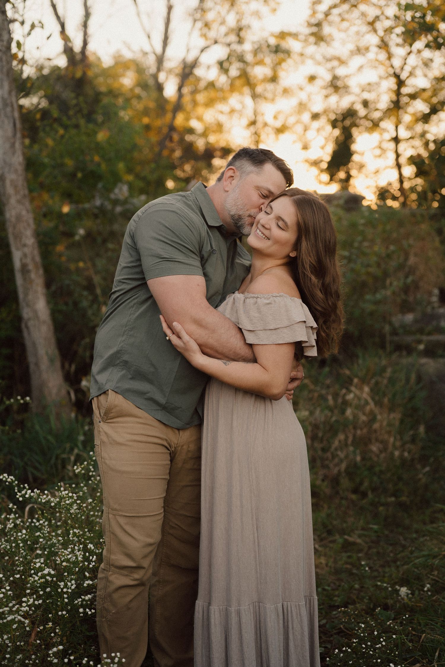 Couple embraces during romantic sunset photoshoot in wooded setting.