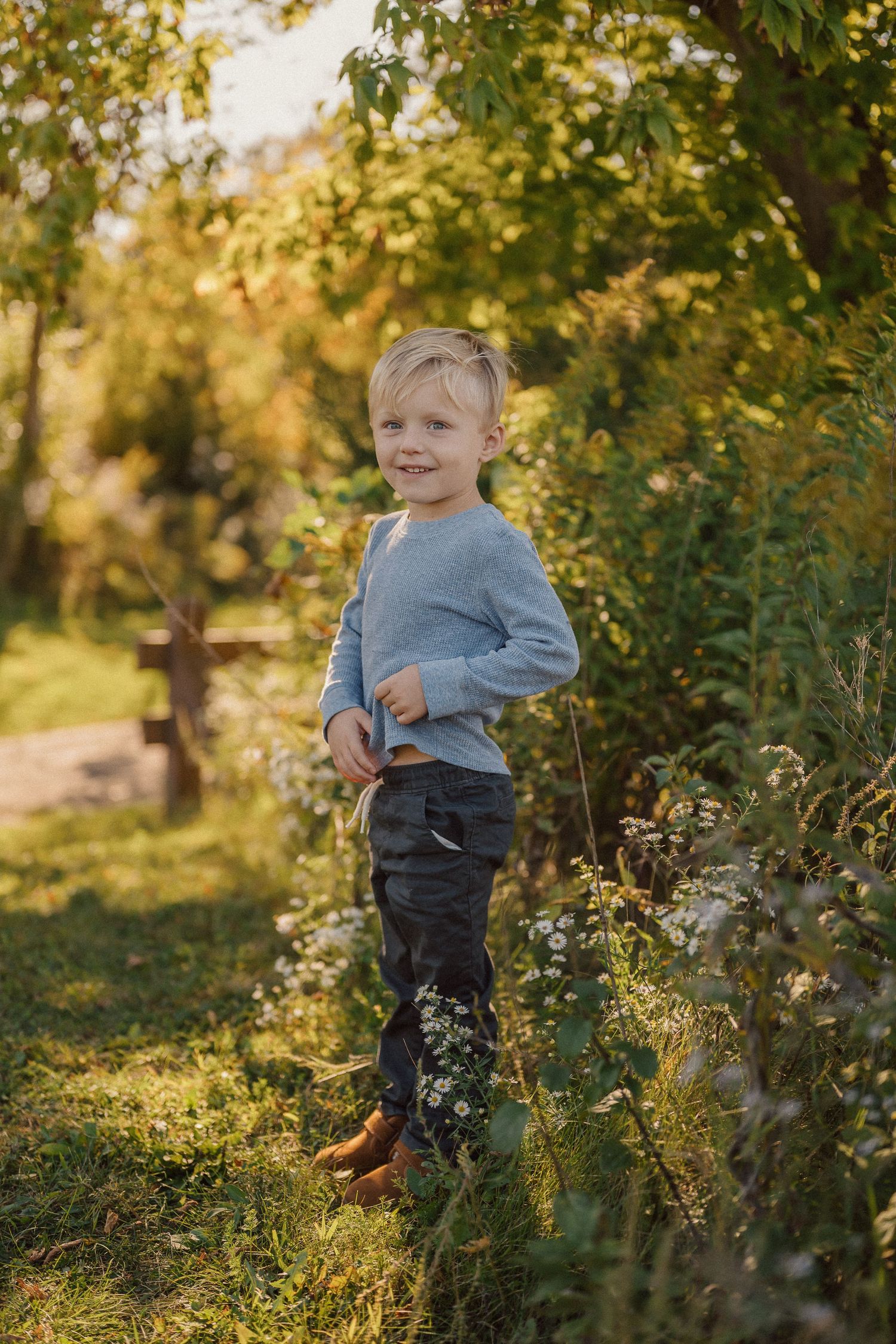 A young child plays in a sunlit garden surrounded by lush greenery and autumn foliage at golden hour.