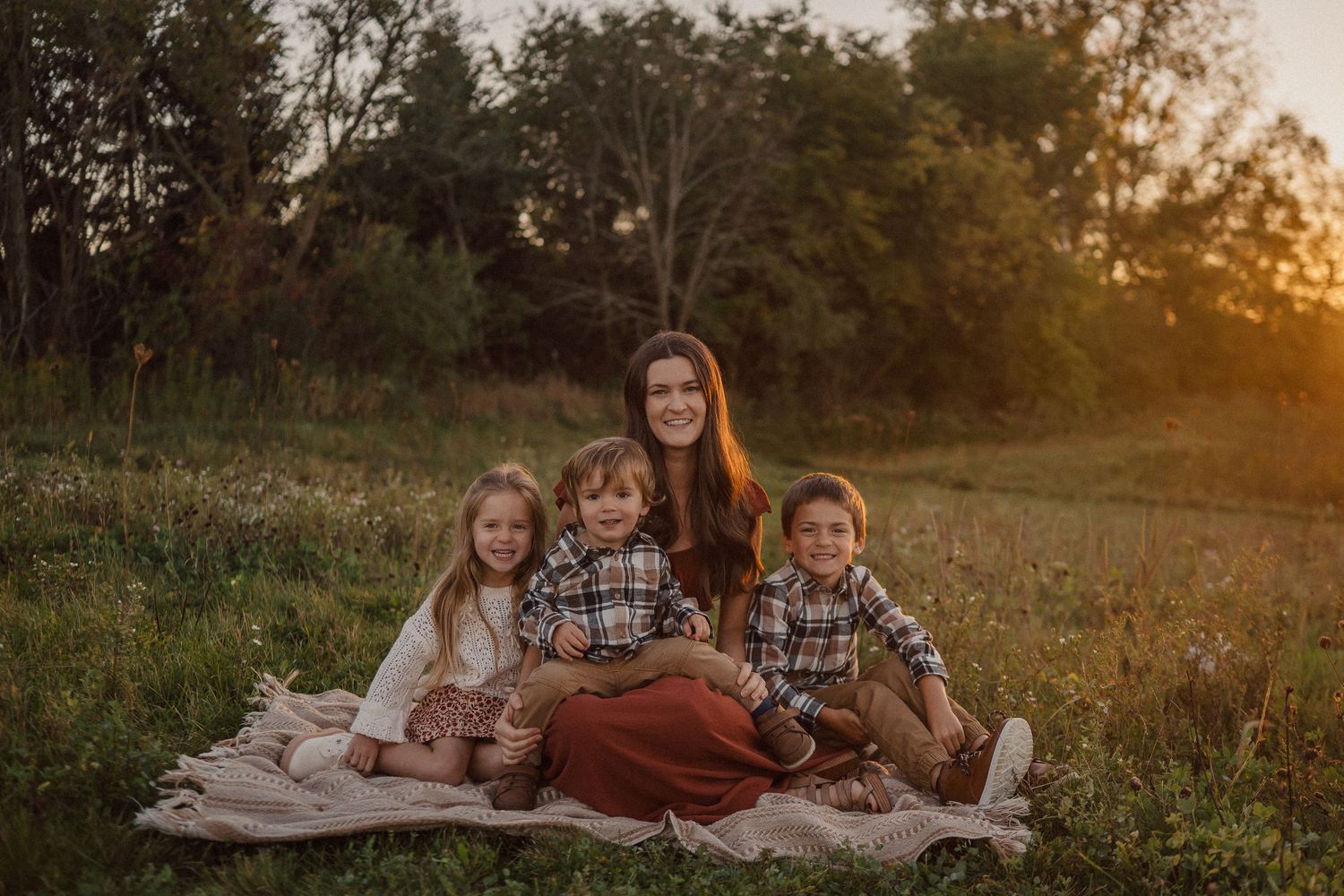 A family sits together on a blanket in a rustic outdoor setting at golden hour.