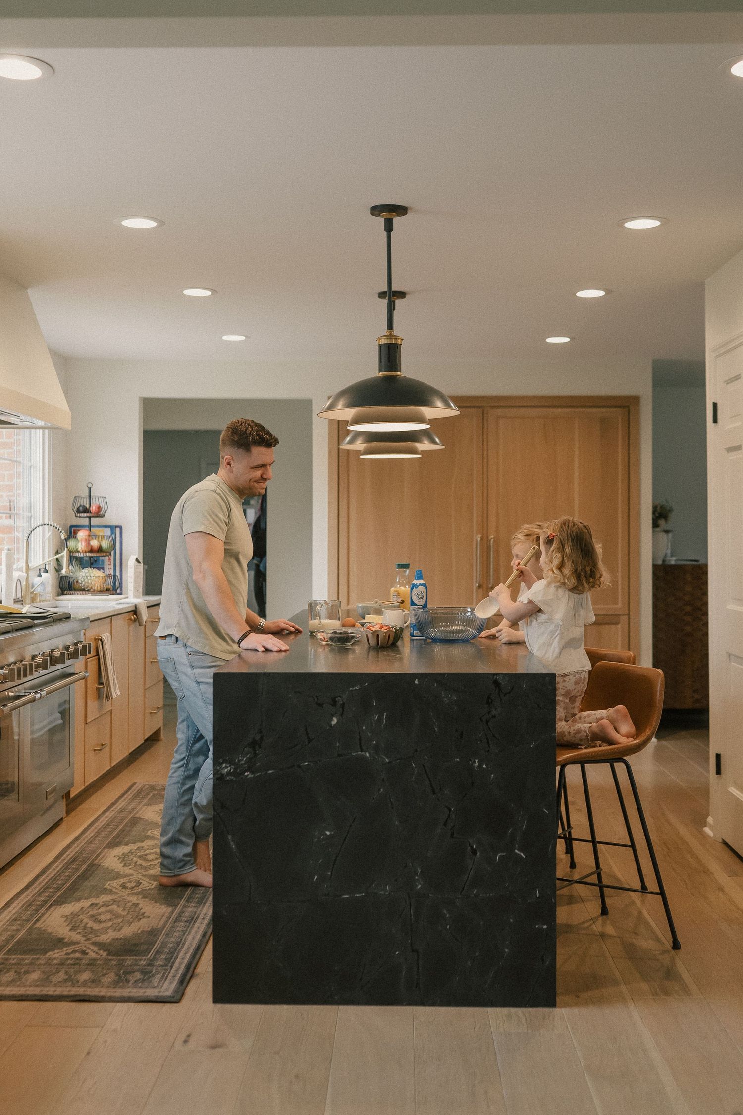 A father and young child enjoy time together at a dark marble kitchen island in a modern home.