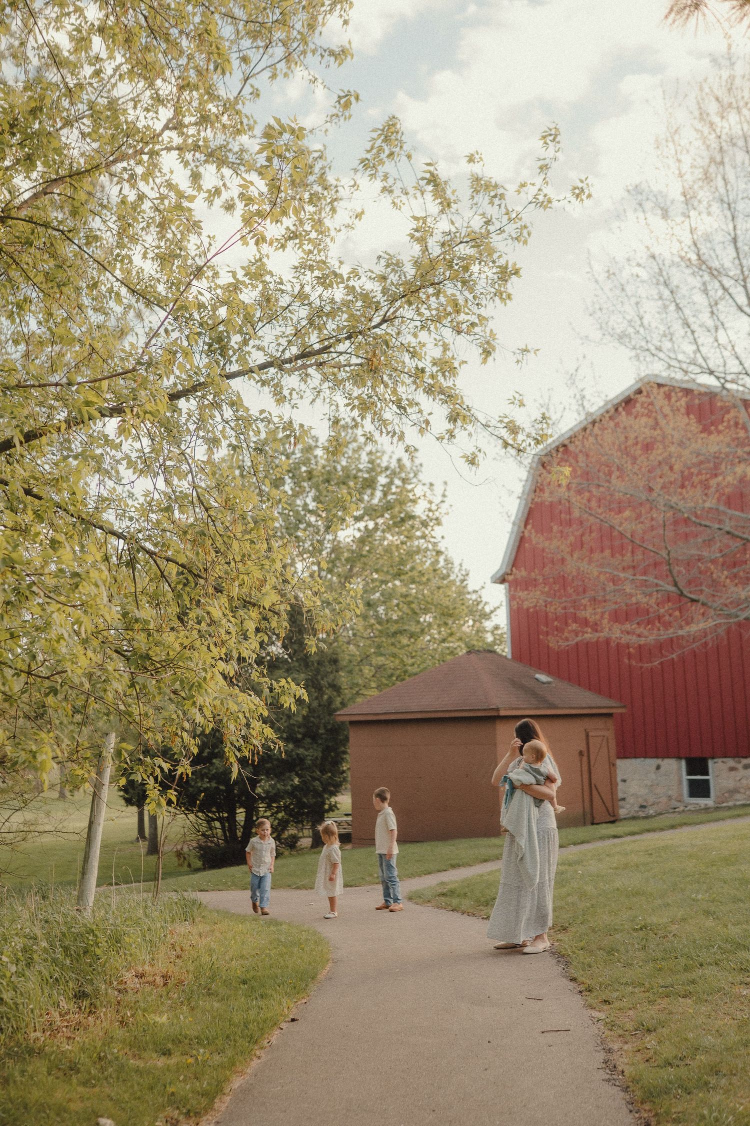 Family walking on a path near a red barn surrounded by autumn trees on a farm.