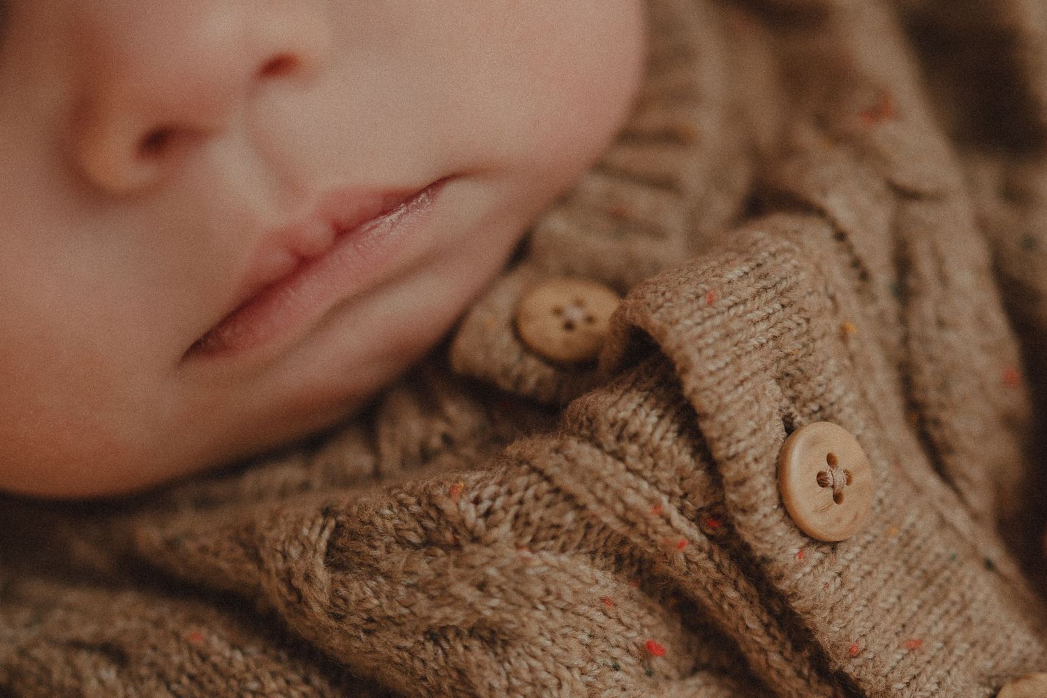 Close-up photo showing lips and partial face wearing warm brown knit sweater with decorative wooden buttons.