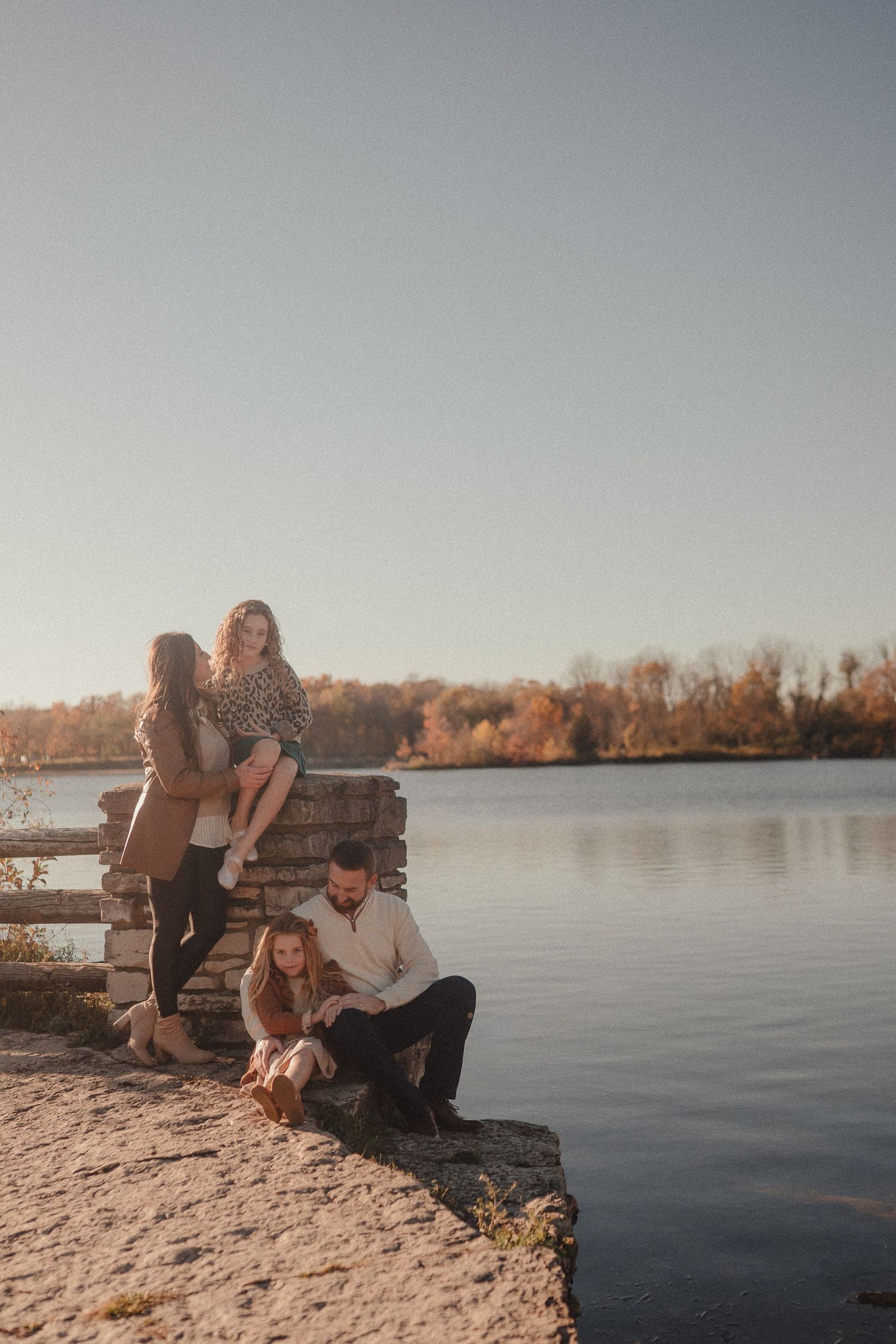 A family sits together on a wooden dock by a serene lake during golden hour.