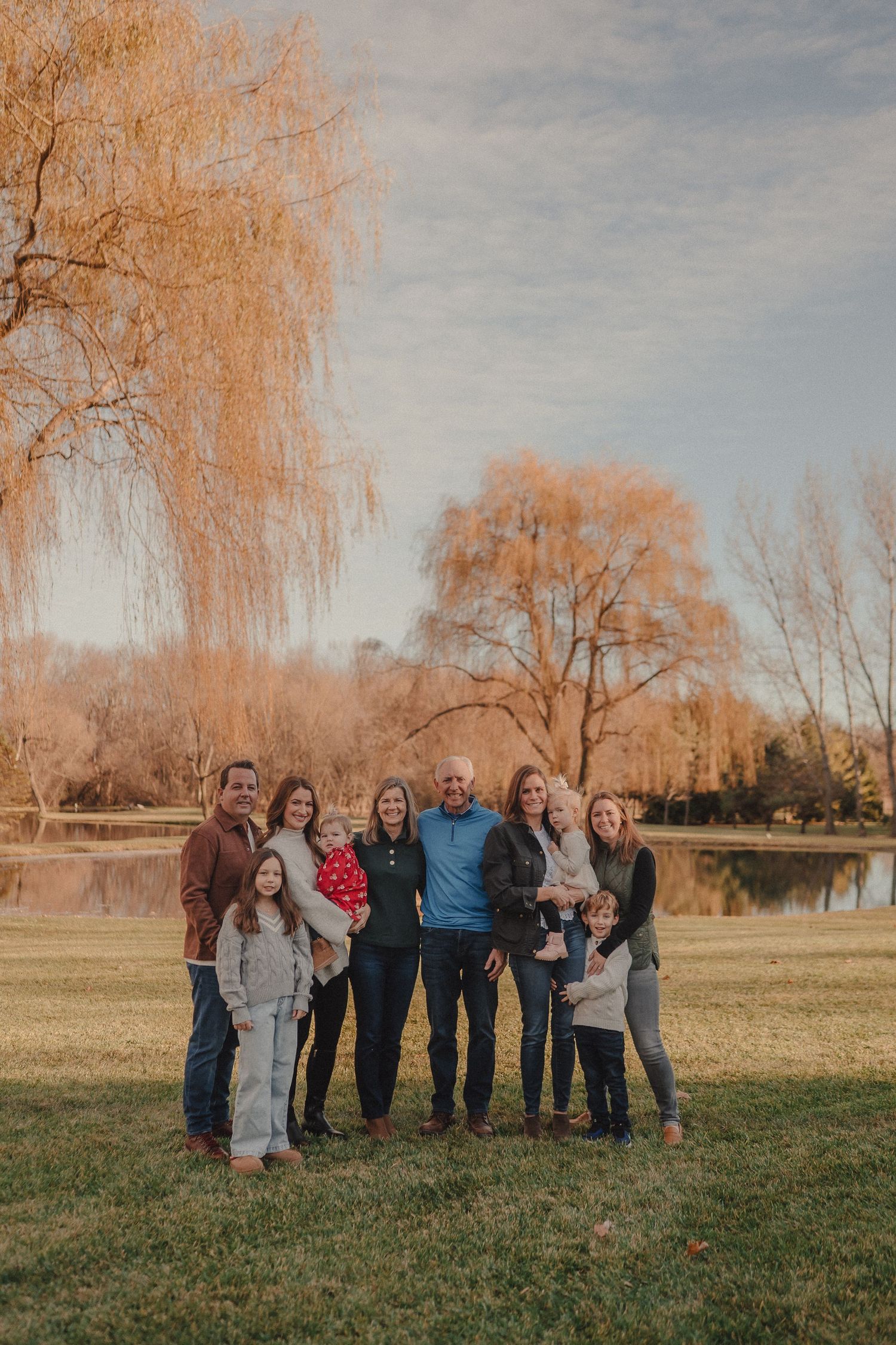 A group gathers outdoors on a grassy field during autumn with bare trees in the background.