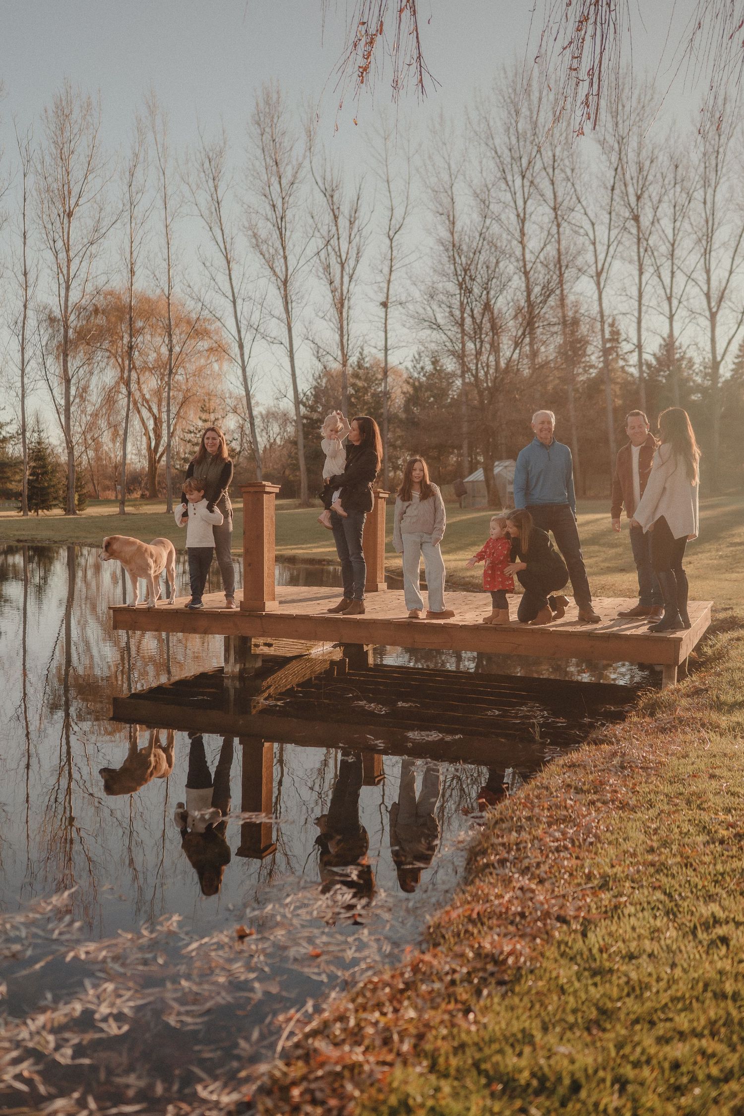People stand together on a wooden dock over a reflective pond during golden hour.