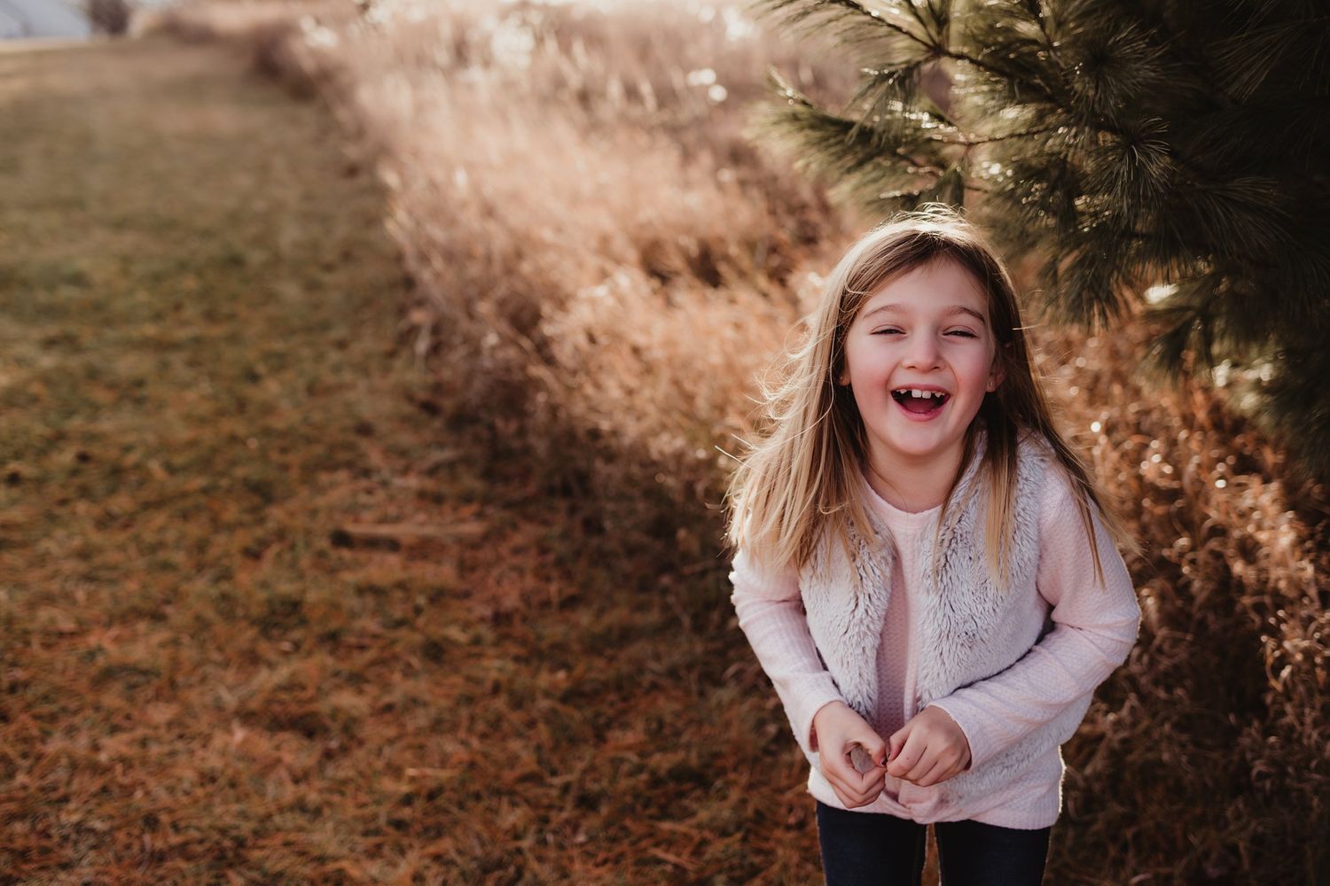 Young child in gray sweater laughing joyfully outdoors.