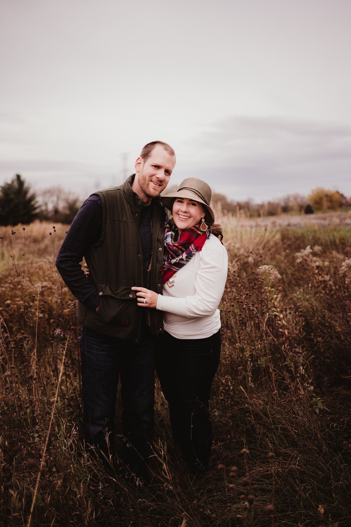 Romantic couple embracing in a rustic field during autumn, wearing cozy outerwear.
