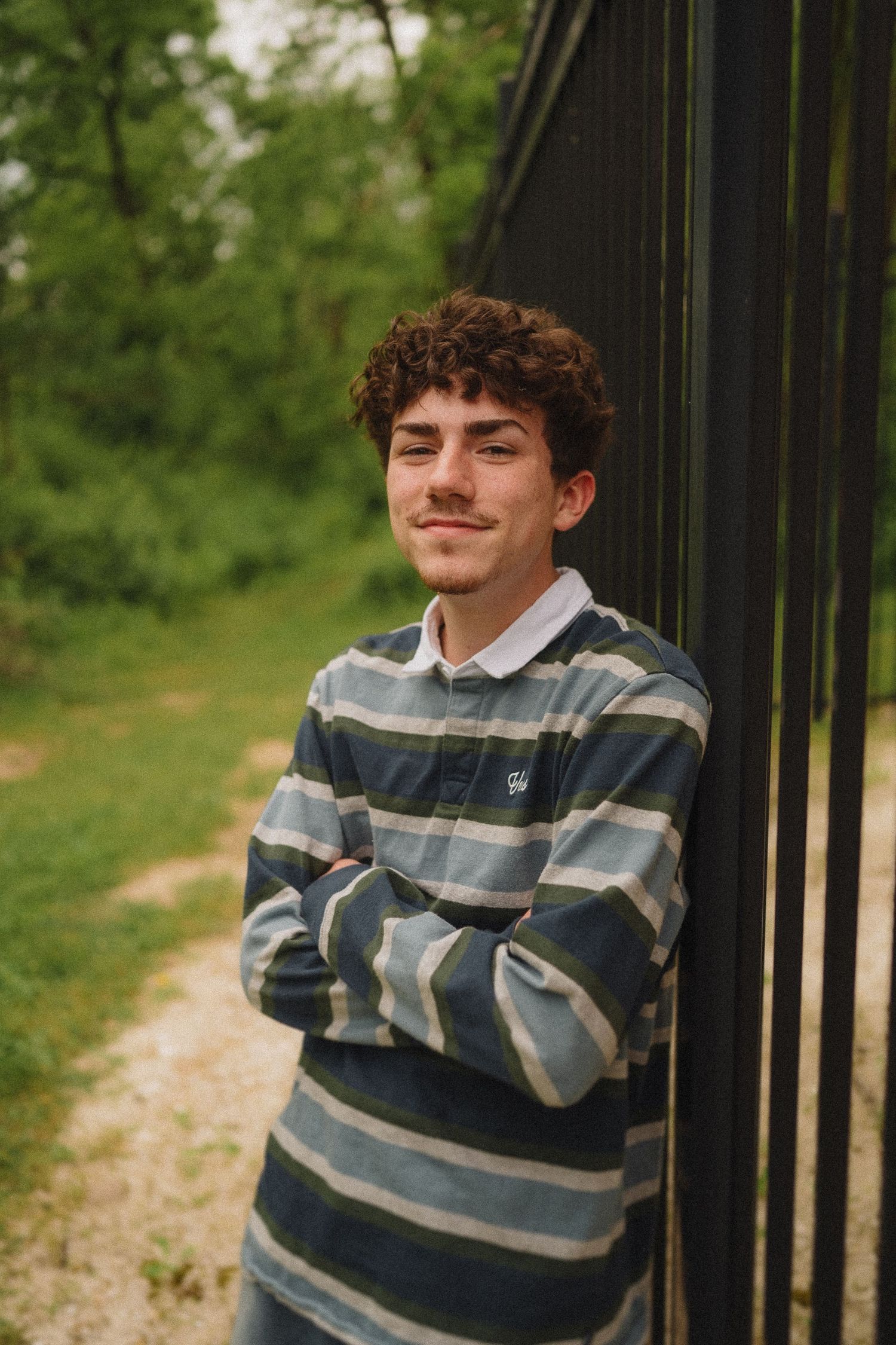 Person wearing striped rugby shirt stands against dark wall outdoors with trees in background.