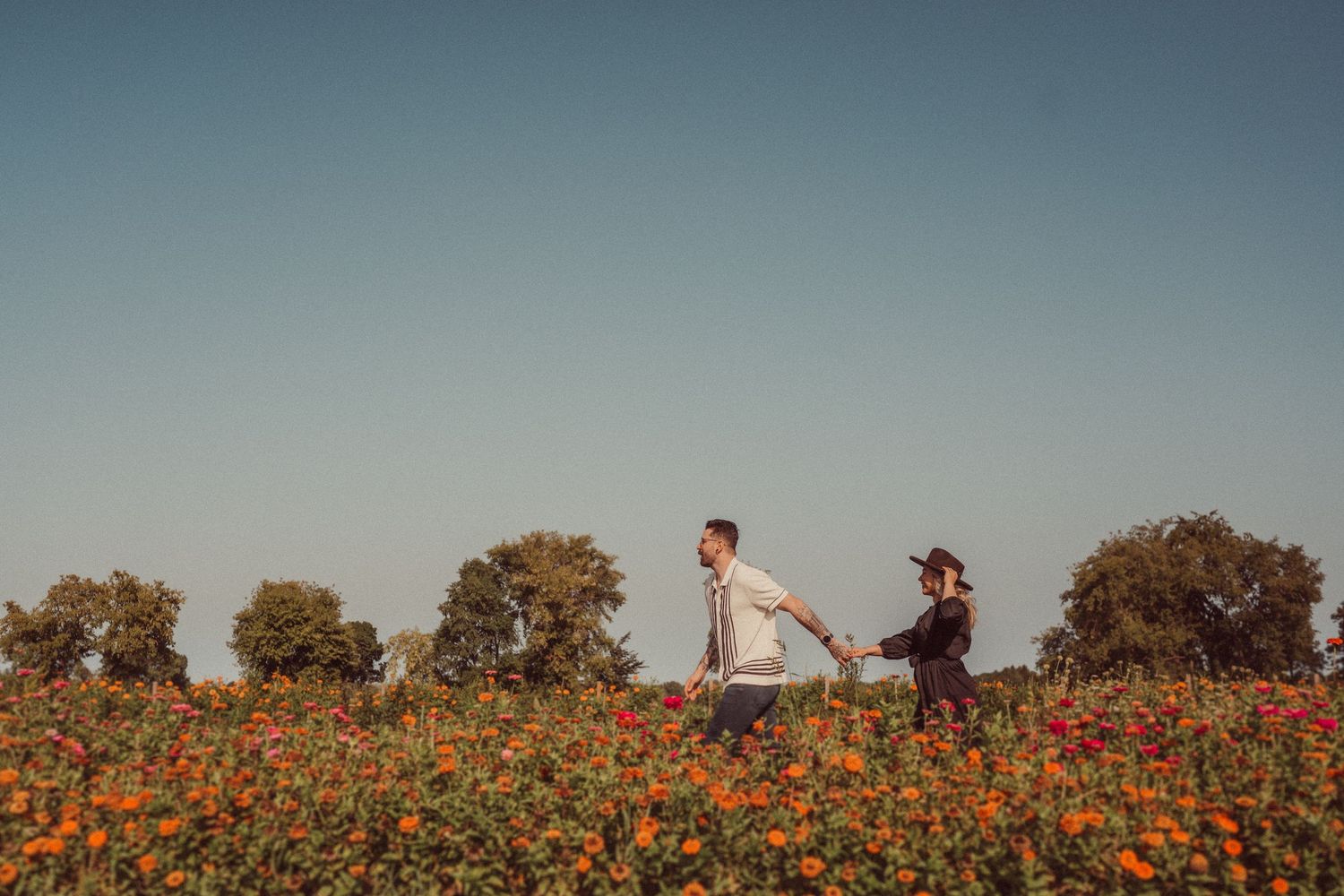 A couple walking together through a colorful wildflower field against a clear sky.