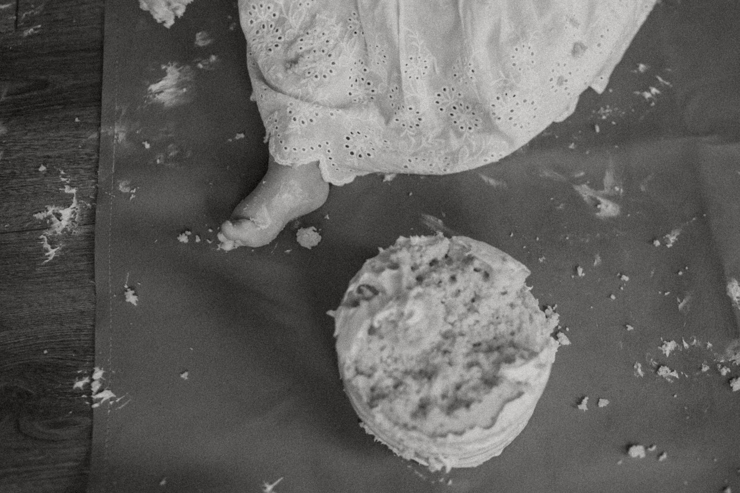 Black and white detail shot of a crumbled cake with scattered crumbs on a dark floor.