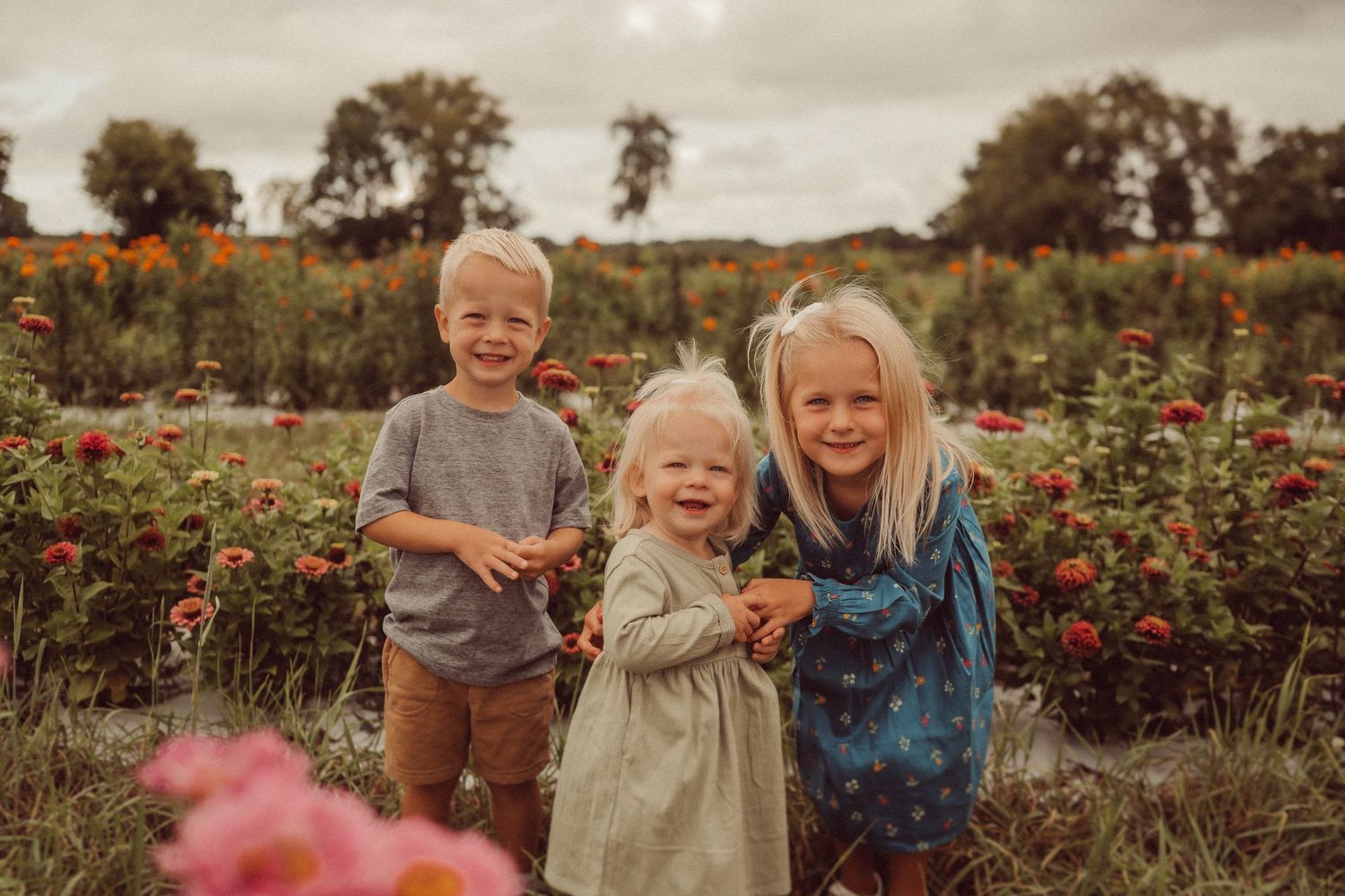 Three children sharing a joyful moment among flowering plants at sunset.