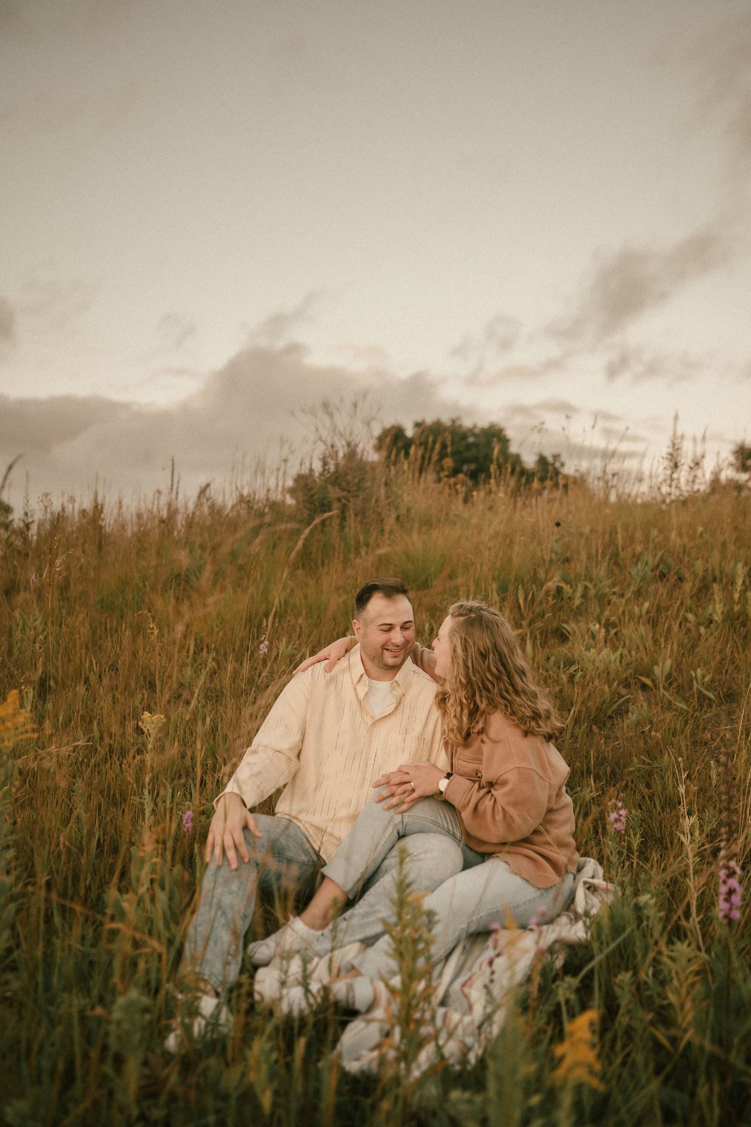 Couple sitting in wildflower meadow during golden hour sunset.
