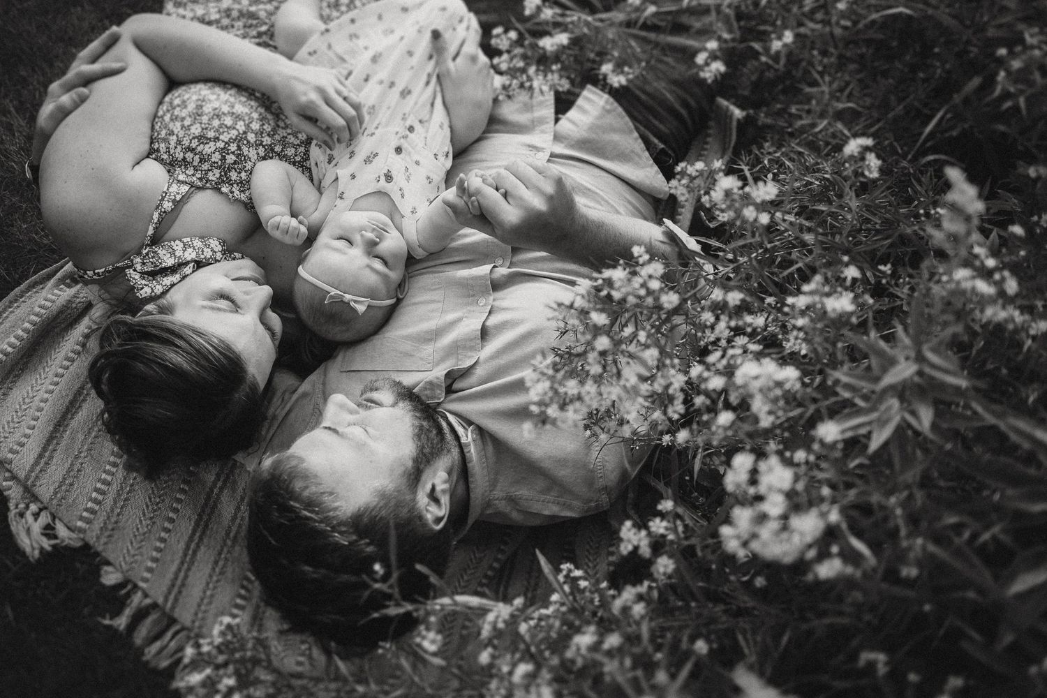 A black and white overhead shot of a family lying among wildflowers.