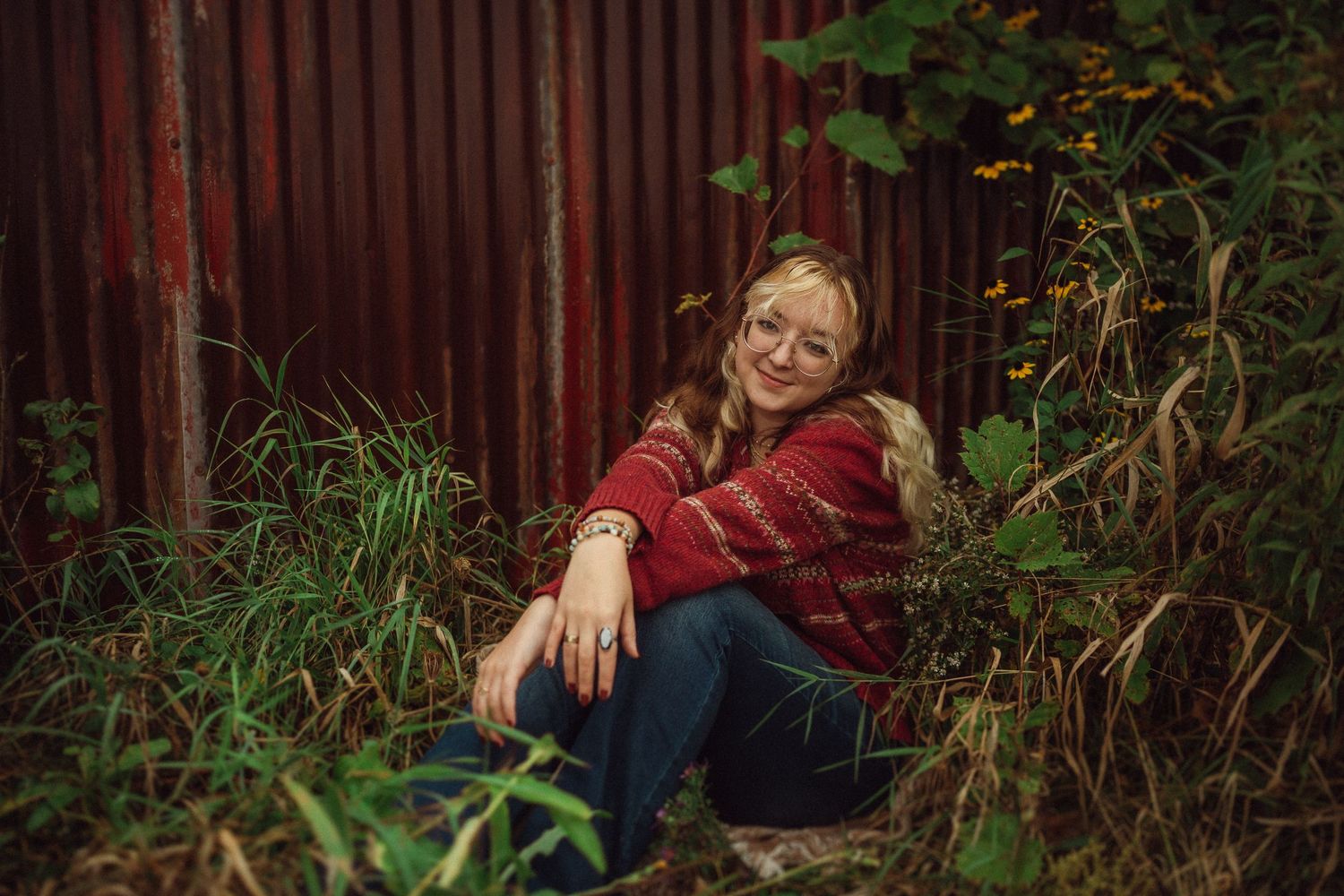 A candid moment captured in a natural setting with overgrown plants and a rustic red wall backdrop.