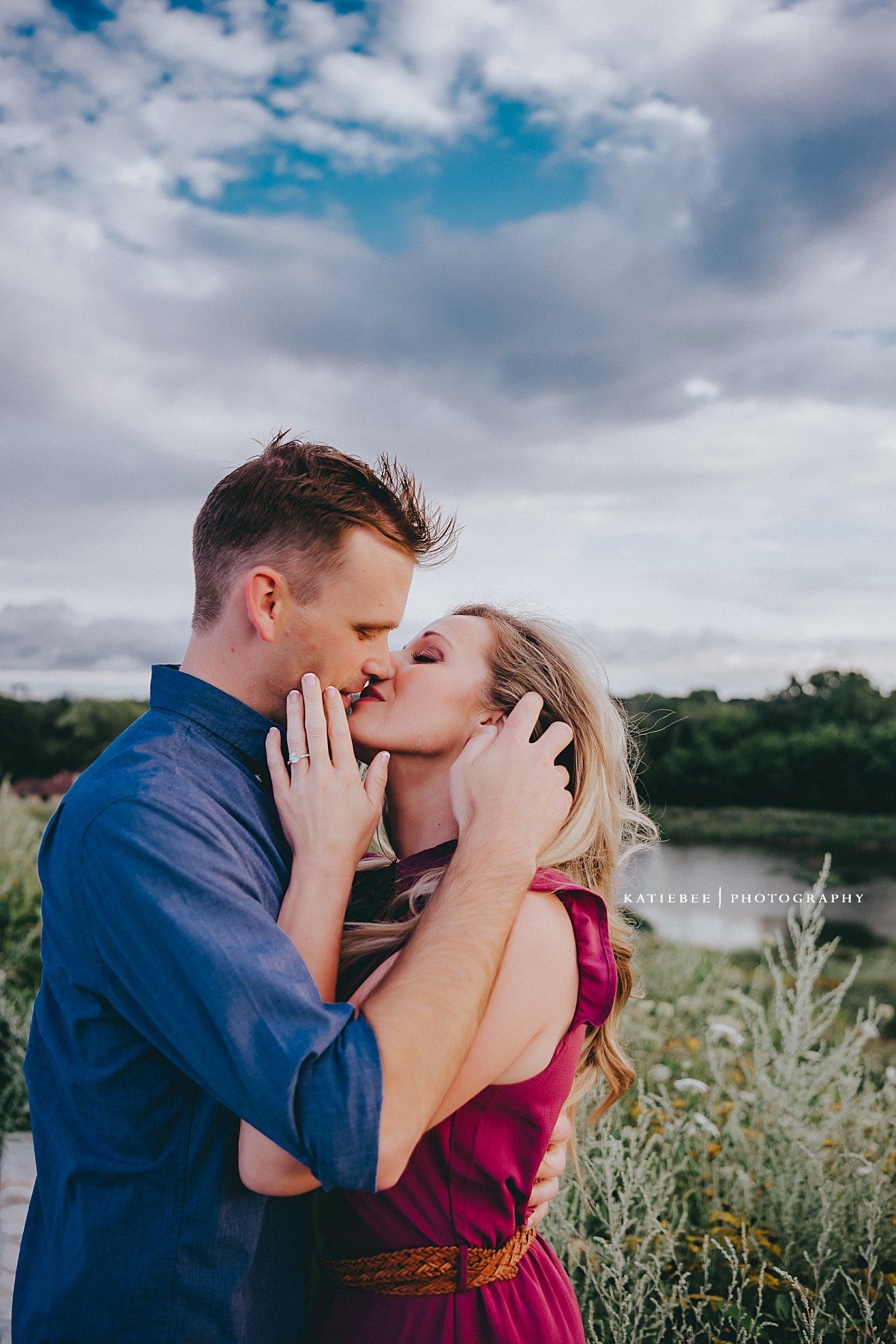 A tender moment between a couple kissing against a cloudy sky background.