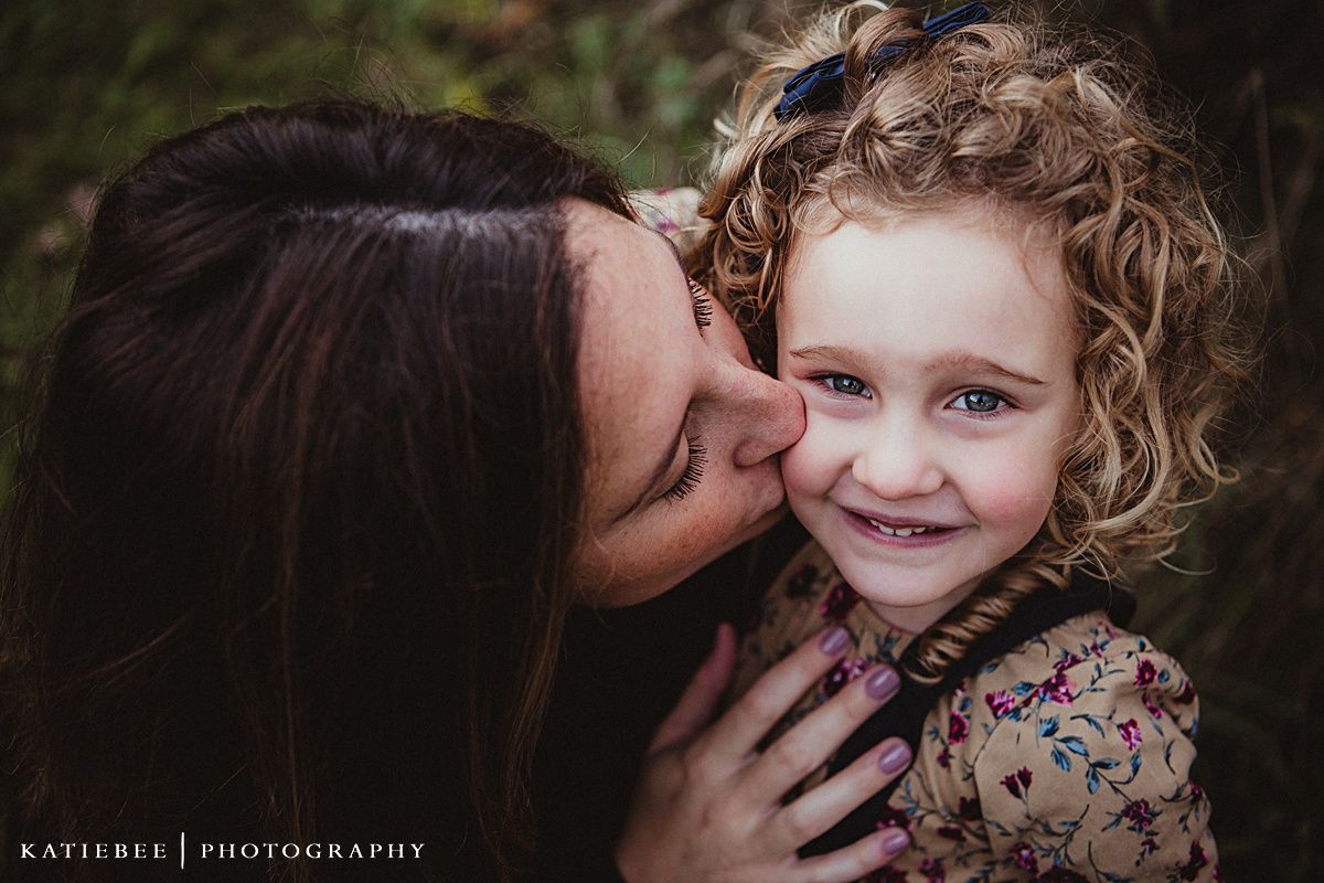 Intimate family portrait captured in soft natural lighting against dark background.