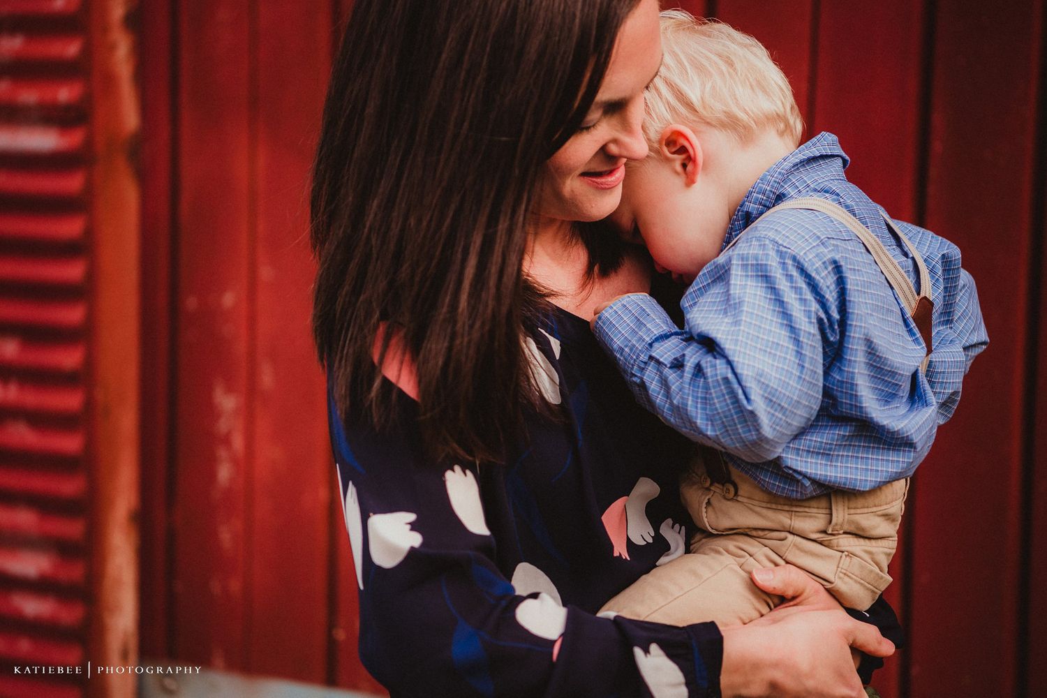 A tender family moment captured against a rustic red barn wall.