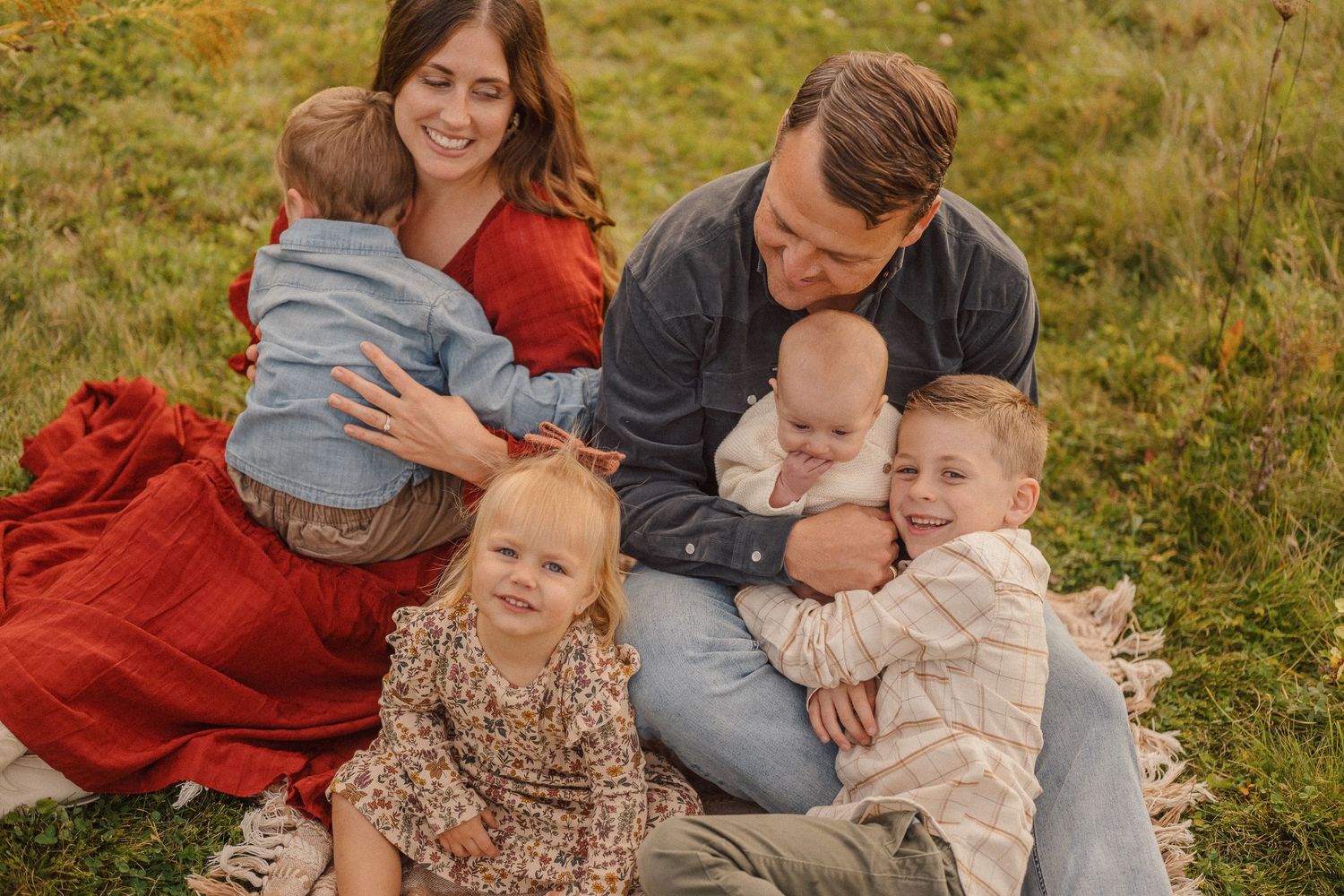 Candid family moment captured on grassy hill during sunset photoshoot.