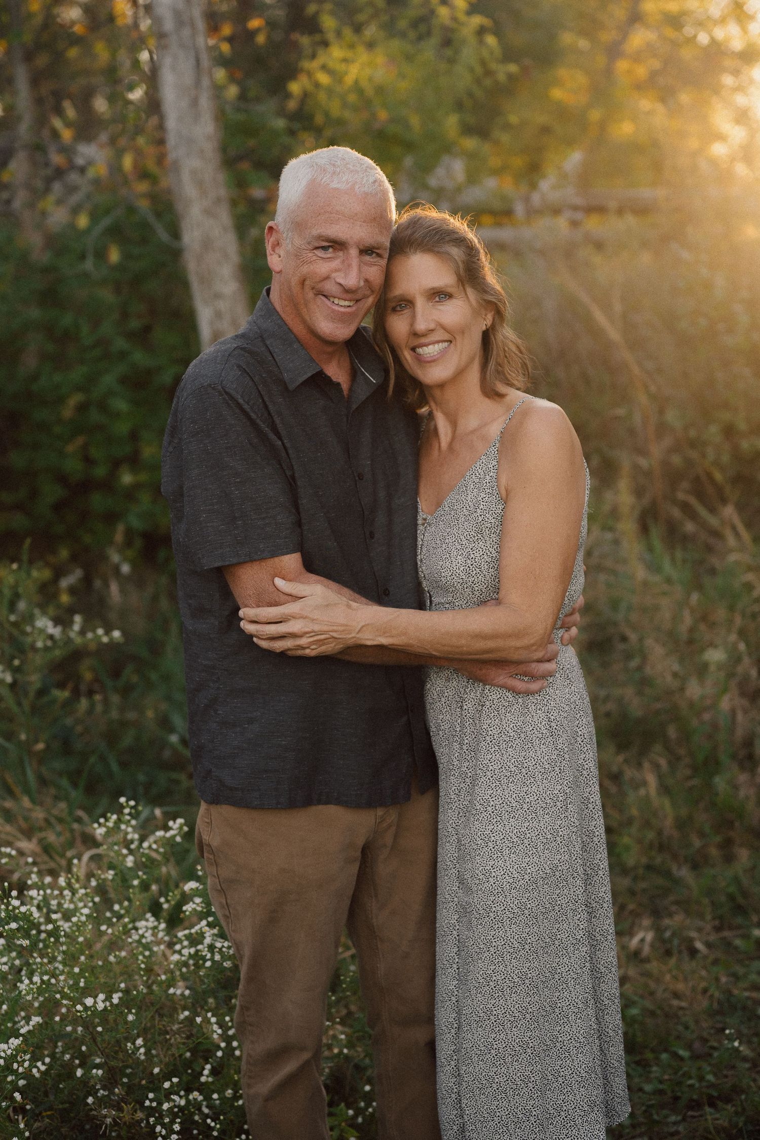 Couple embracing outdoors during golden hour with trees and natural lighting.