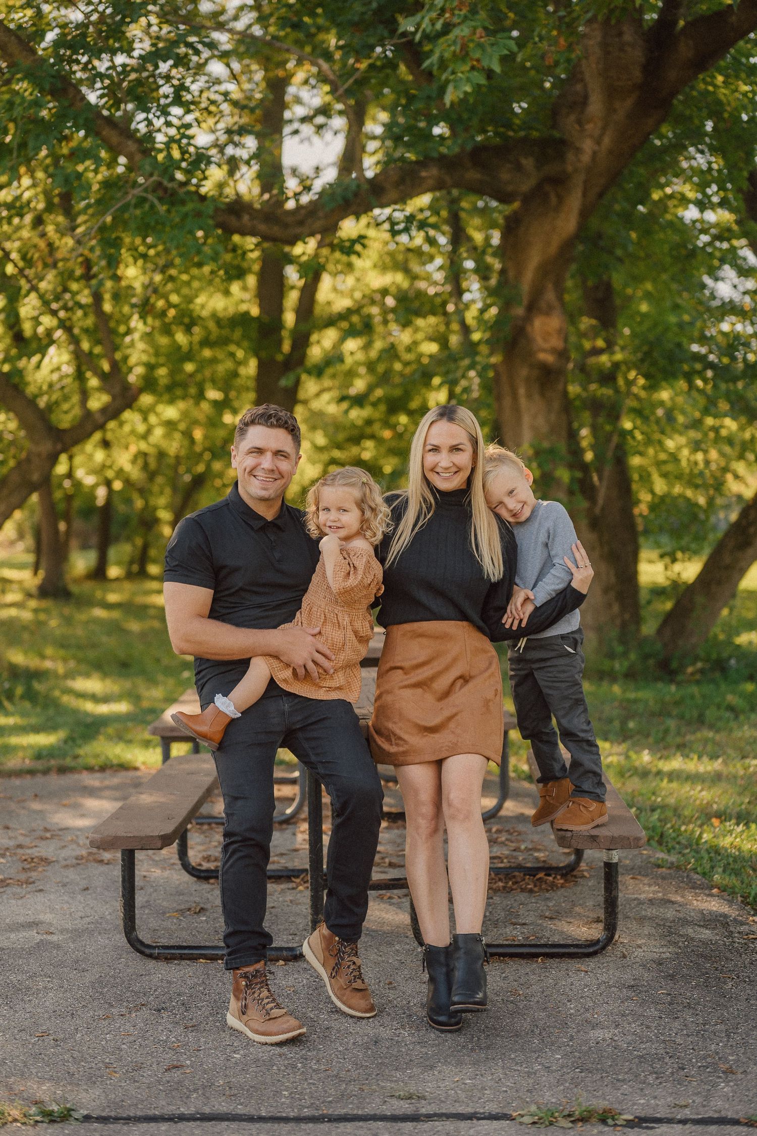 Family sits together on a park bench surrounded by autumn trees in warm evening light.